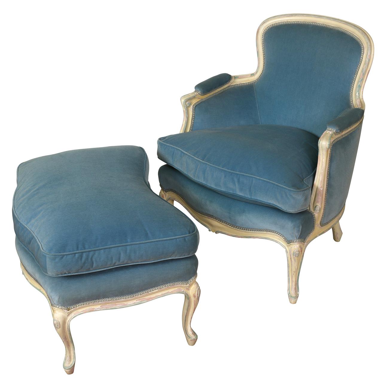 An elegant bergere with ottoman in the Louis XV style, having an exposed wood frame in a grayish white finish with soft blue accents. This sturdy and comfortable is upholstered in a stunning blue velvet.  The bergere has a tight back and loose seat