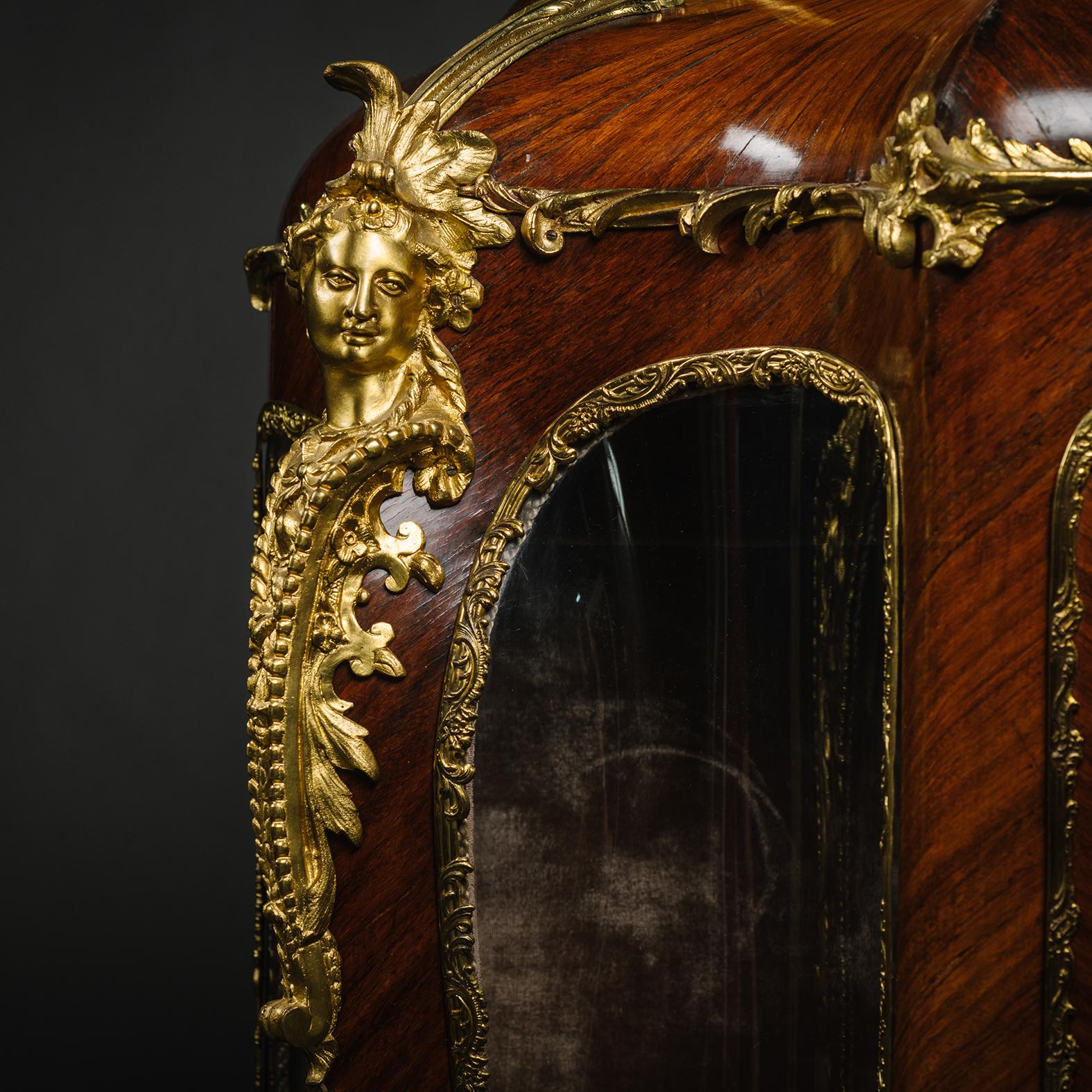 A Louis XV Style Gilt-Bronze Mounted Vernis Martin Vitrine Cabinet.

The spreading pediment centred by a rocaille clasp and flanked by exotic busts. The central three-quarter glazed door is flanked by recessed glazed panels and sides. Each above a