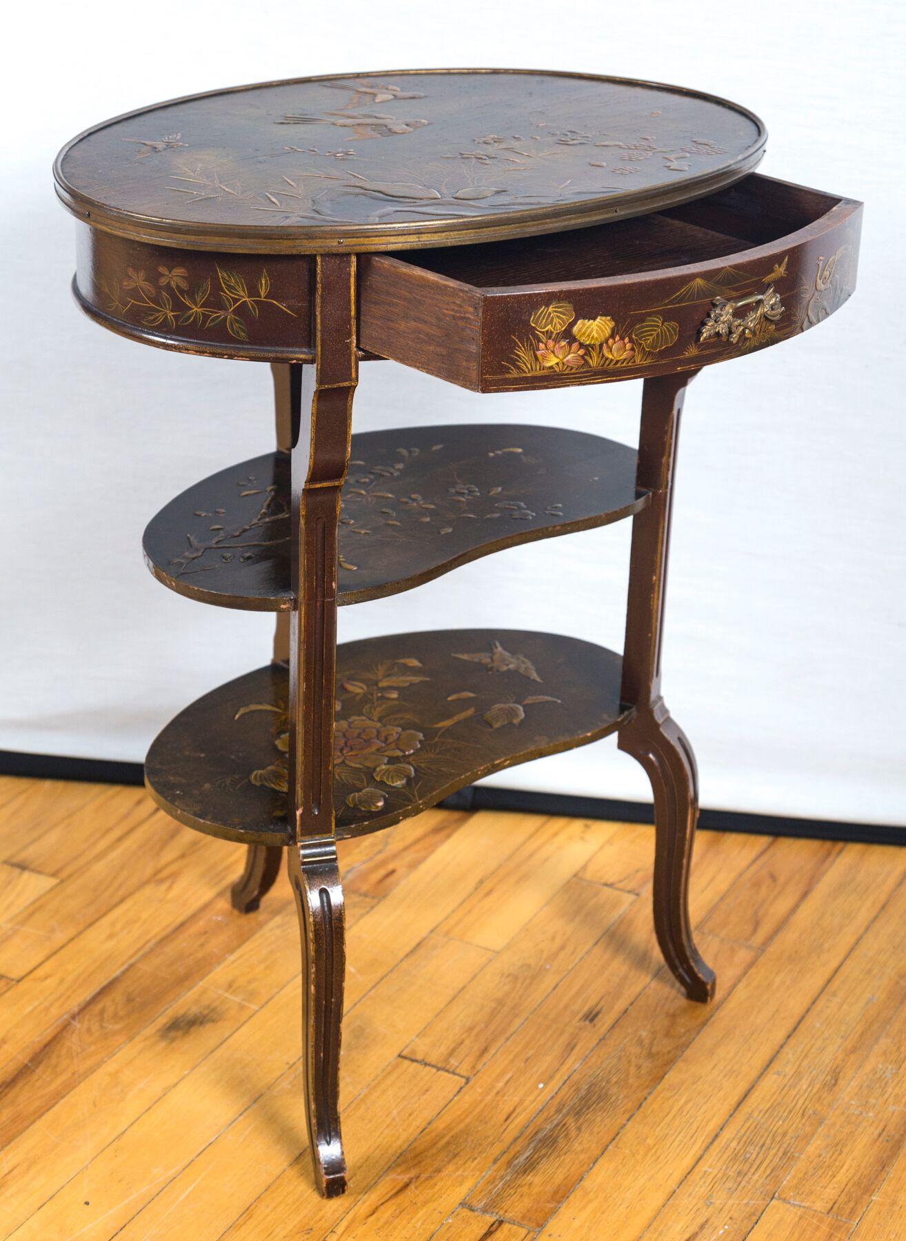 A Louis XV style occasional table hand painted with birds, insects, foliage, and flowers. An oval top over incurvate legs joined by 2 shelves as stretchers. A single drawer, with original decorative hardware.