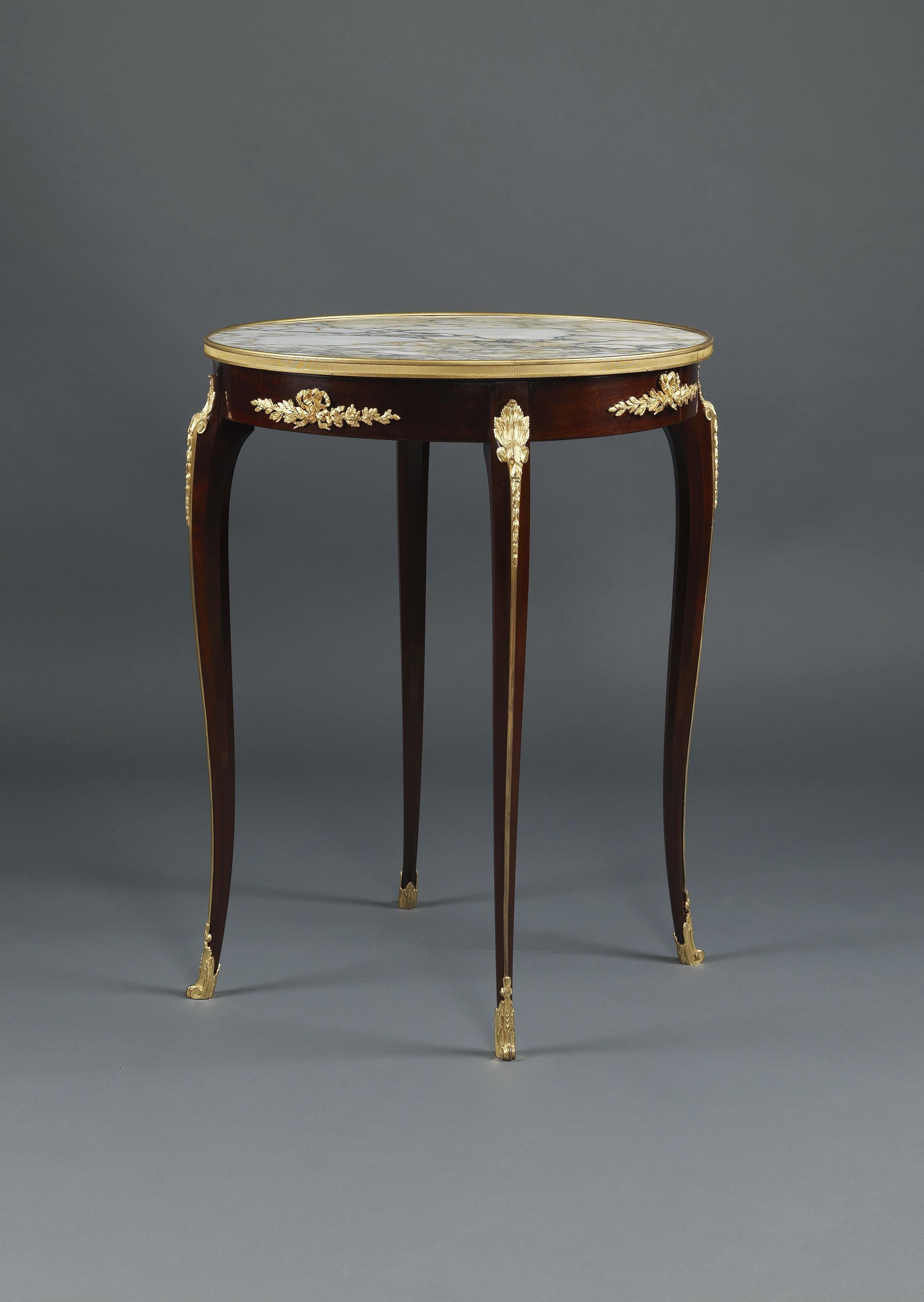 A Louis XV style gilt-bronze mounted mahogany Gueridon with a marble top.

French, circa 1890.

The circular marble top within a gilt-bronze band above a frieze with gilt-bronze ribbon tied foliate mounts.