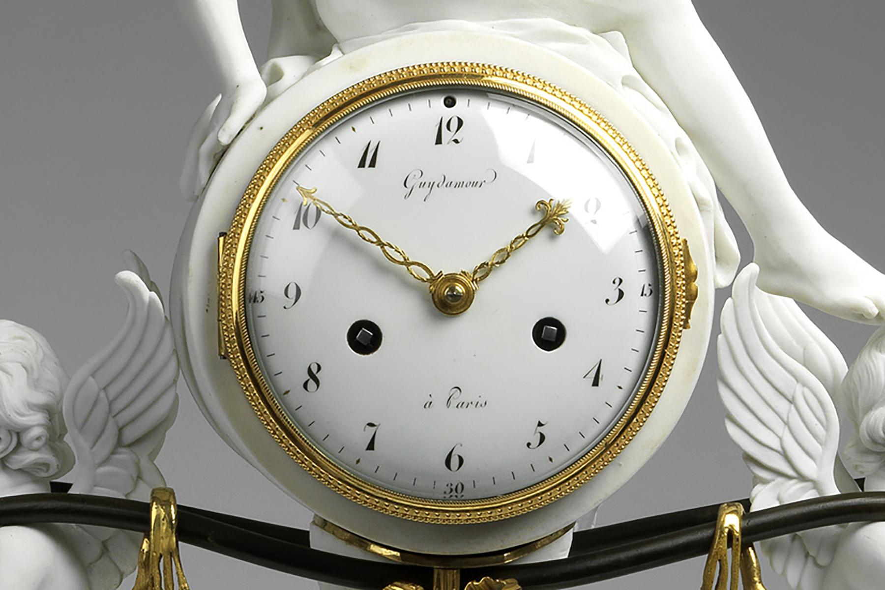 The circular white enamel dial with black numerals, inscribed Guydamour à Paris, with striking movement contained within a round case; surmounted by a woman, her right hand raised clasping a goblet, her body being partially draped in fabric; the