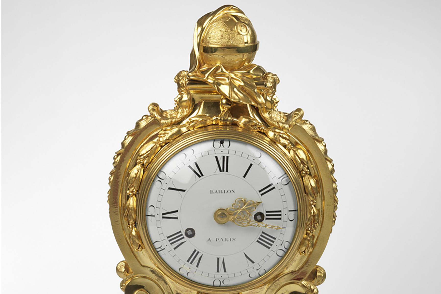 The white enamel dial is set within an ormolu drum-shaped case with a bead and reel border and signed Baillon à Paris. The drum is raised on scrolls, above a shaped rectangular base with a pierced ormolu grill, with a lion’s mask holding golden