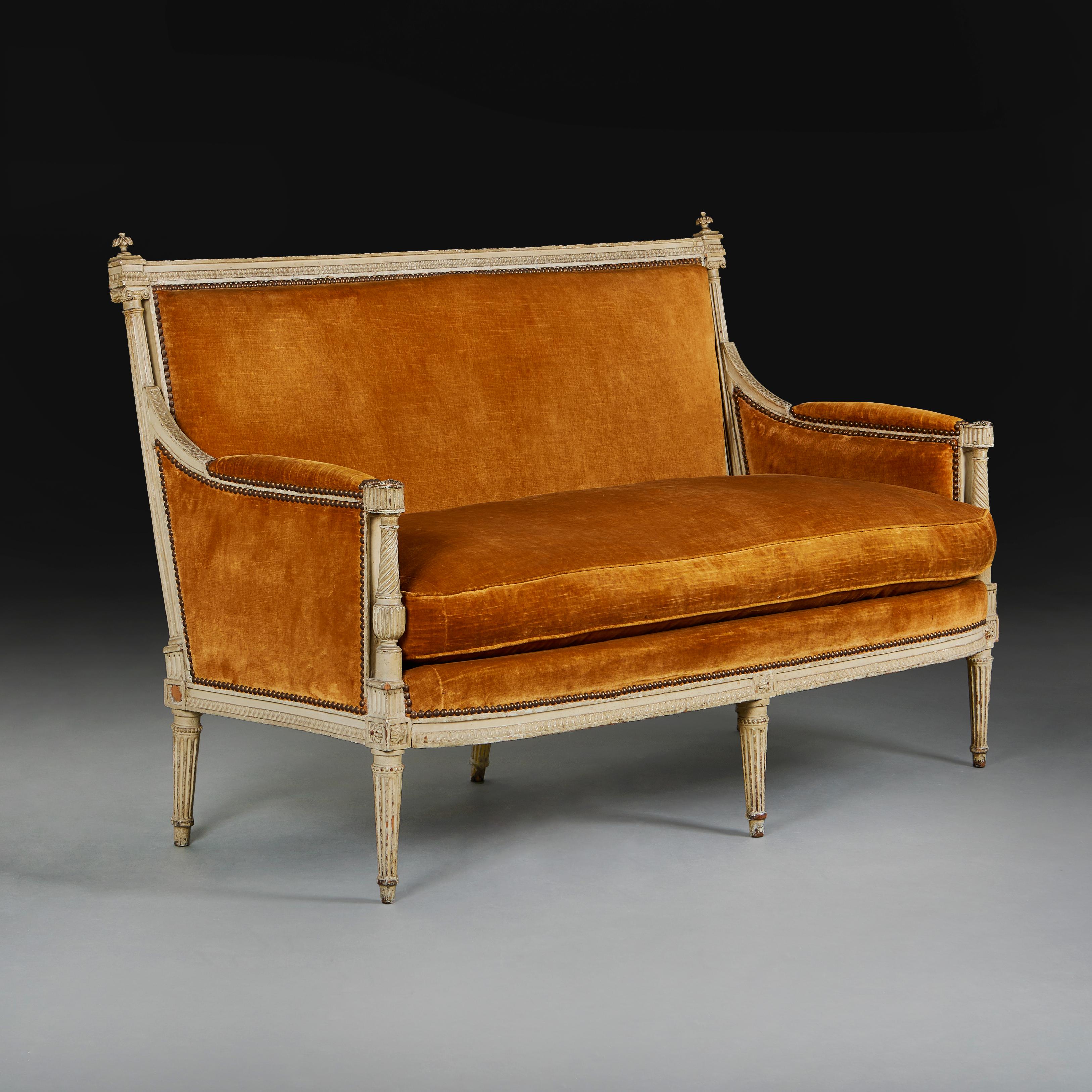 Fino sofá de estilo Luis XVI tapizado en terciopelo naranja quemado, apoyado en un armazón de madera de haya con molduras de hojas y dardos, columnas jónicas y brazos retorcidos que se prolongan hasta unas patas cónicas y estriadas.