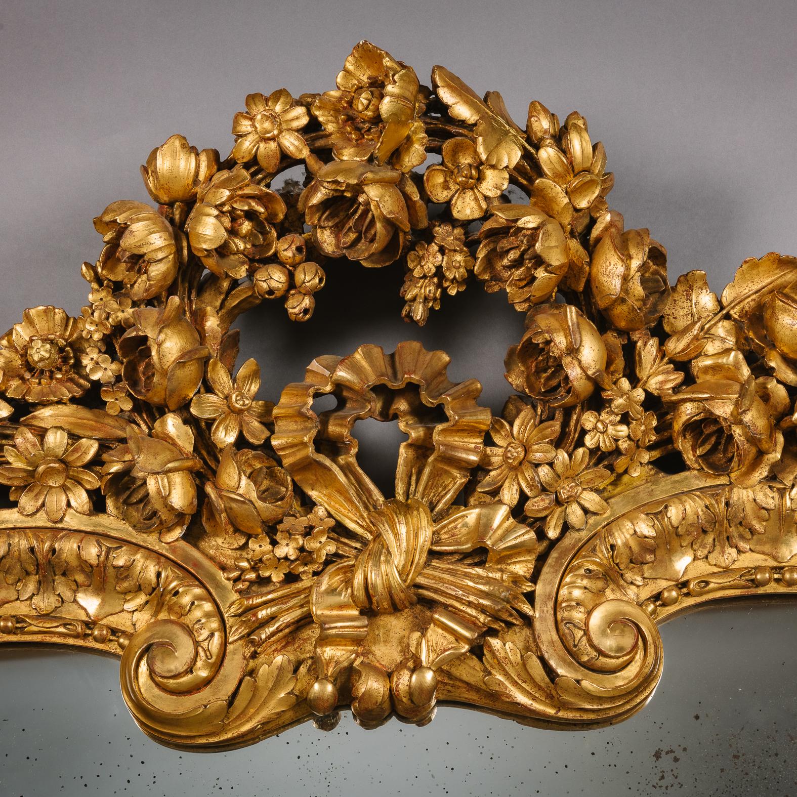 A Louis XVI style carved giltwood and gesso overmantel mirror.

The arched mirror plate set within a scroll capped acanthus and lotus-leaf frame, with an acanthus and foliate carved apron centred by a shell, surmounted by a ribband-tied arched