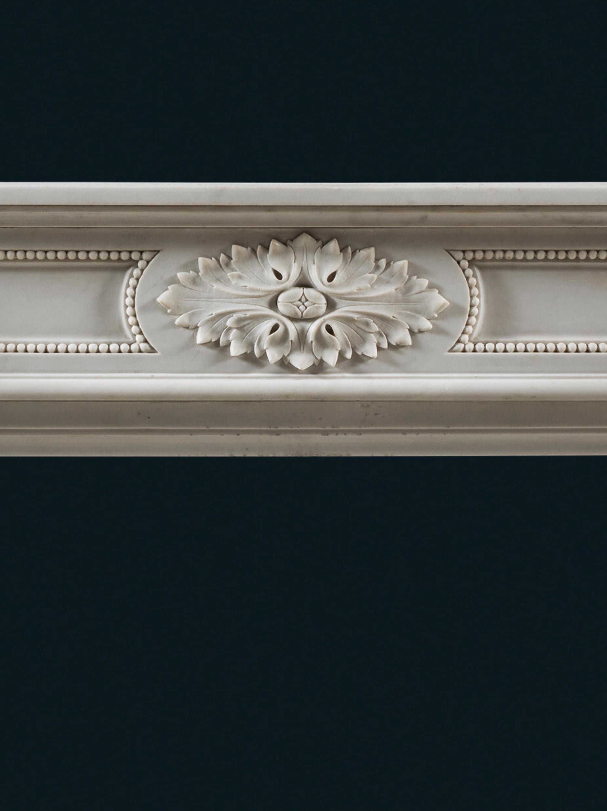 Cheminée de style Louis XVI du 19ème siècle en marbre statuaire avec des glissières en fonte d'origine

Des feuilles d'acanthe entourent les blocs d'angle circulaires, soutenus par des jambages cannelés effilés. La frise est centrée par un détail