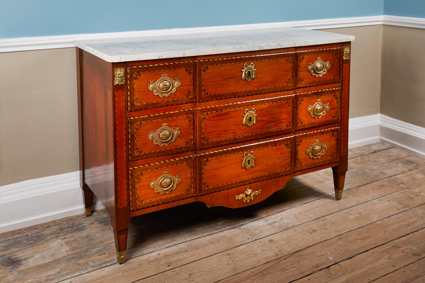 A Louis XVI style commode, 19th century, France, veneered with tulip and kingwood, the three drawers with ring-pull handles and escutcheons, with ebony and boxwood stripes, on tapered legs capped with brass feet, with marble top.