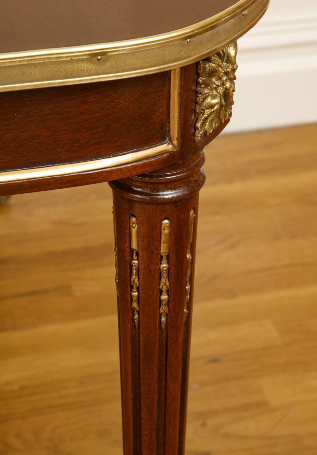 A French Louis XVI style mahogany dining table in the manner of Jansen, with stop fluted tapering legs headed by rosettes, and bronze trim along the surface and castors.
This table includes two leaves, each 24