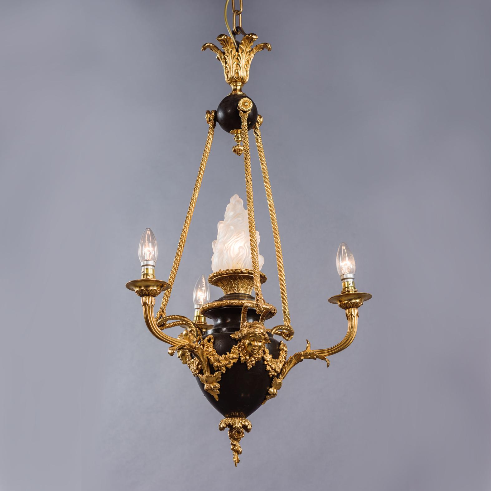 A Louis XVI Style Gilt and Patinated Bronze Four-Light Chandelier. 

The chandelier has a gilt-bronze acanthus cast corona above a patinated orb, with writhen suspensions rods suspending a patinated bronze urn embellished with gilt-bronze masks and