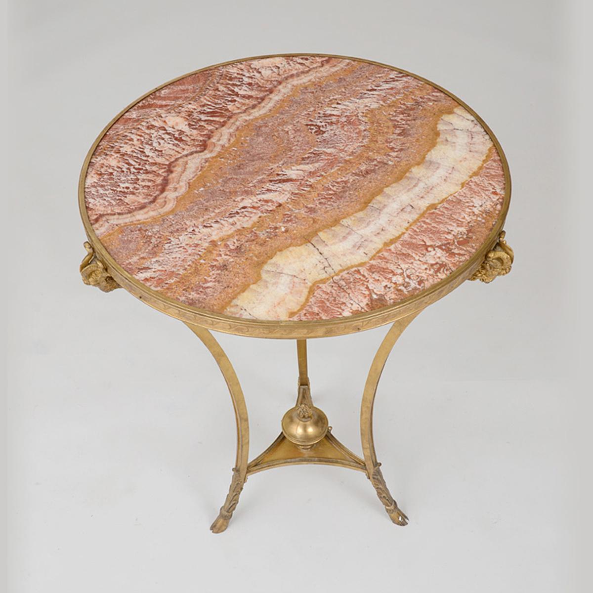 A fine quality Louis XVI style gilt bronze and marble-top Guéridon.
The circular agate-inset top within a wave border, raised on incurved supports with ram masks, continuing to the tripartite stretcher centered by a flaming urn, ending on hoof