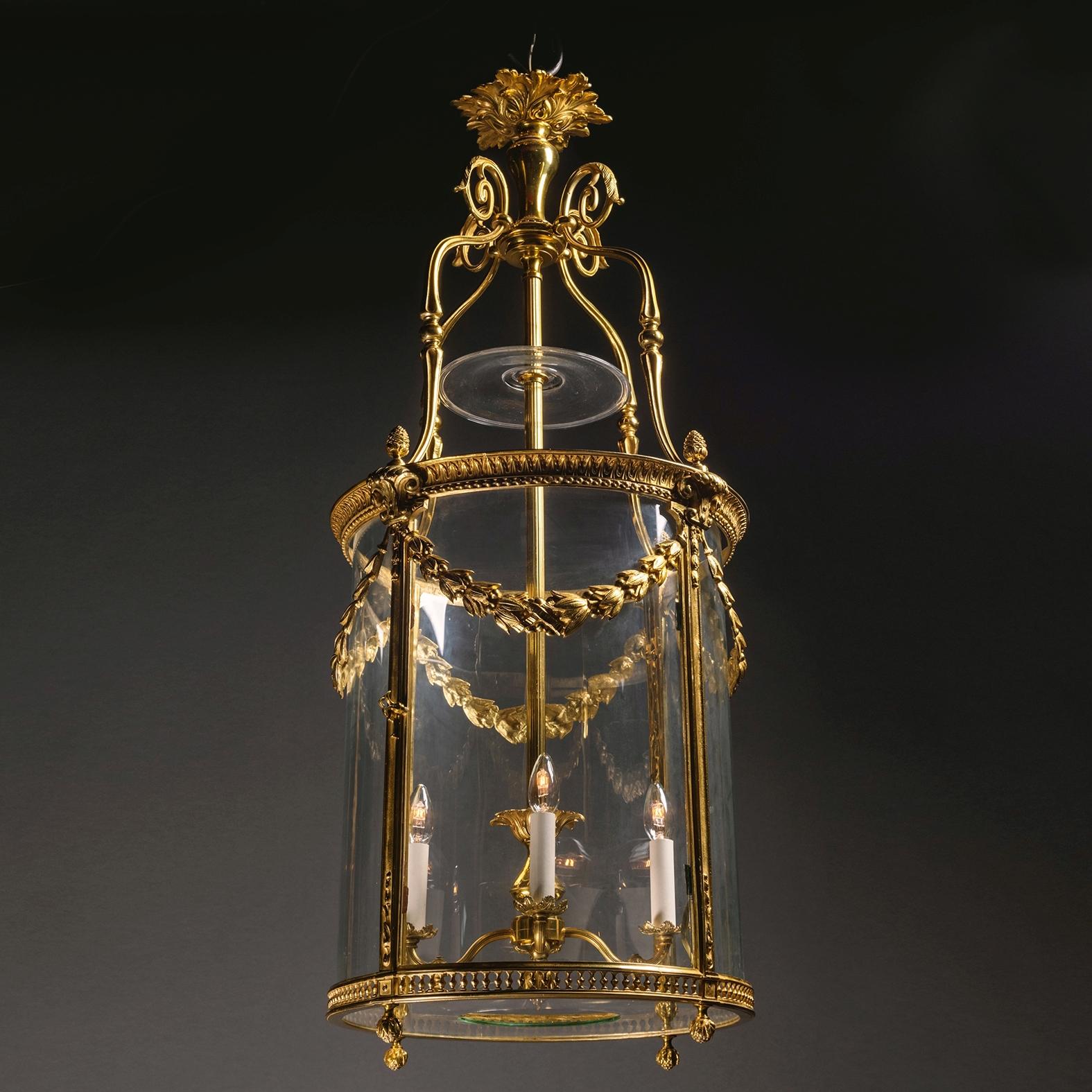 Lanterna cilindrica a quattro luci in stile Luigi XVI in bronzo dorato.  

Questa lanterna ha una forma cilindrica con montanti a coste che sorreggono una cornice con bordi a foglie dure e volute floreali, sormontata da terminali a ghianda.  Lo