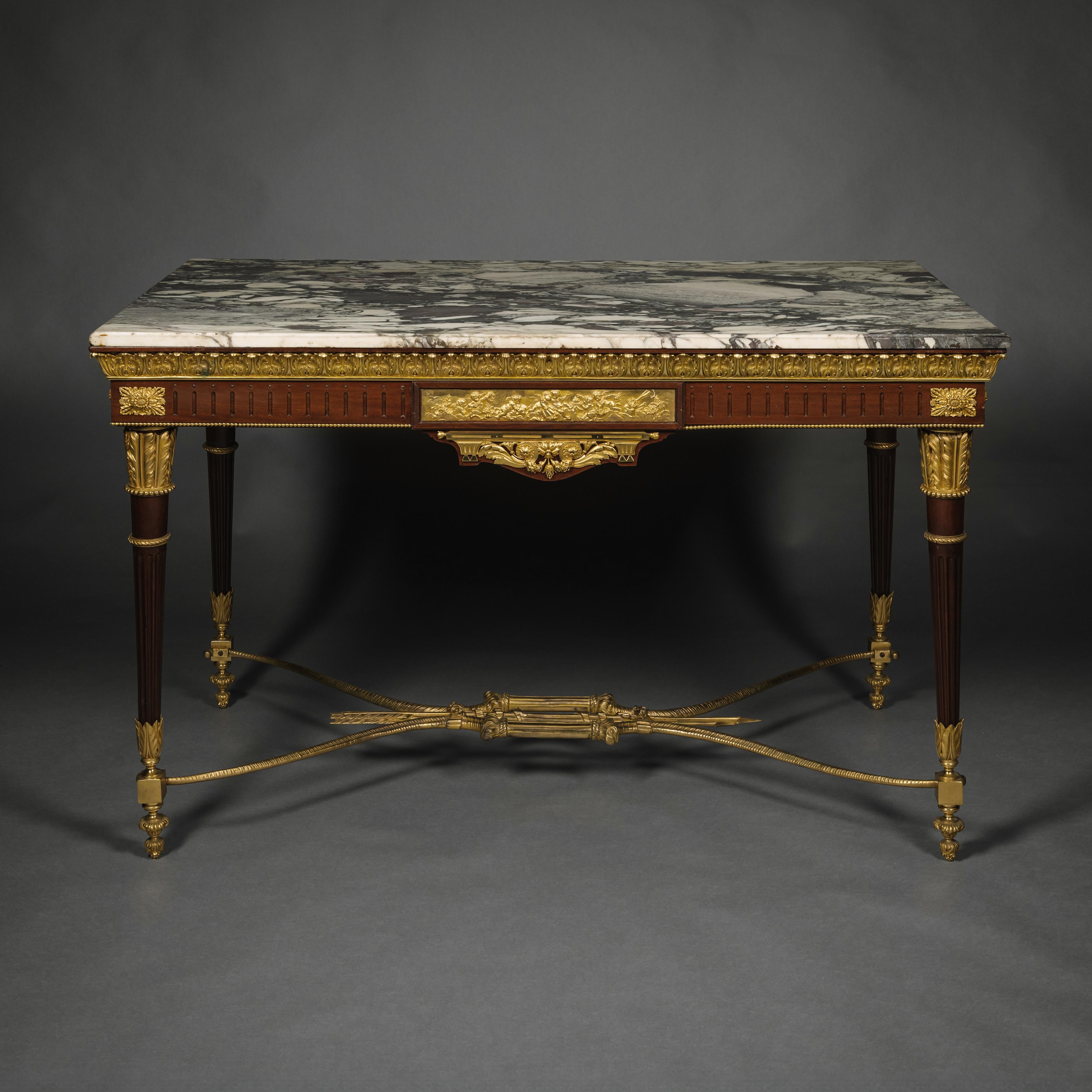 Ein vergoldeter Mahagoni-Mitteltisch im Louis-XVI-Stil mit Bronzebeschlägen.

Der Tisch mit einer Marmorplatte aus Villefranche de Conflent mit zart violetten Mustern auf weißem Grund. Unter der Marmorplatte befindet sich ein vergoldeter Bronzerand