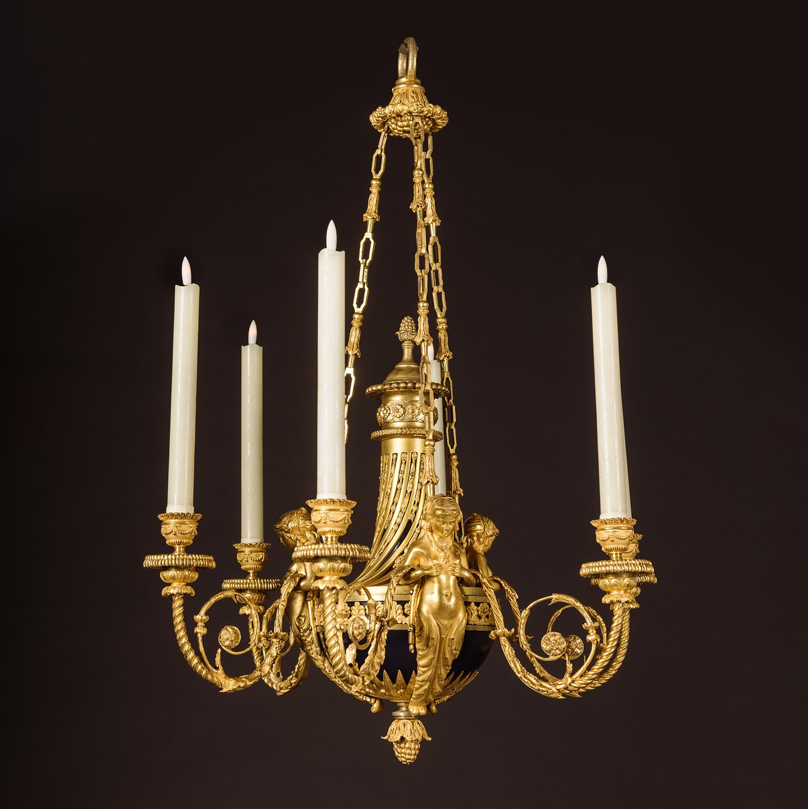 Lampadario a sei luci 'Aux Termes' in stile Luigi XVI in bronzo dorato.

La ciotola centrale in tole dipinte di blu con coperchio scanalato a spirale e terminale a melograno. Modellato con tre figure a forma di cariatide che tengono in mano rami a