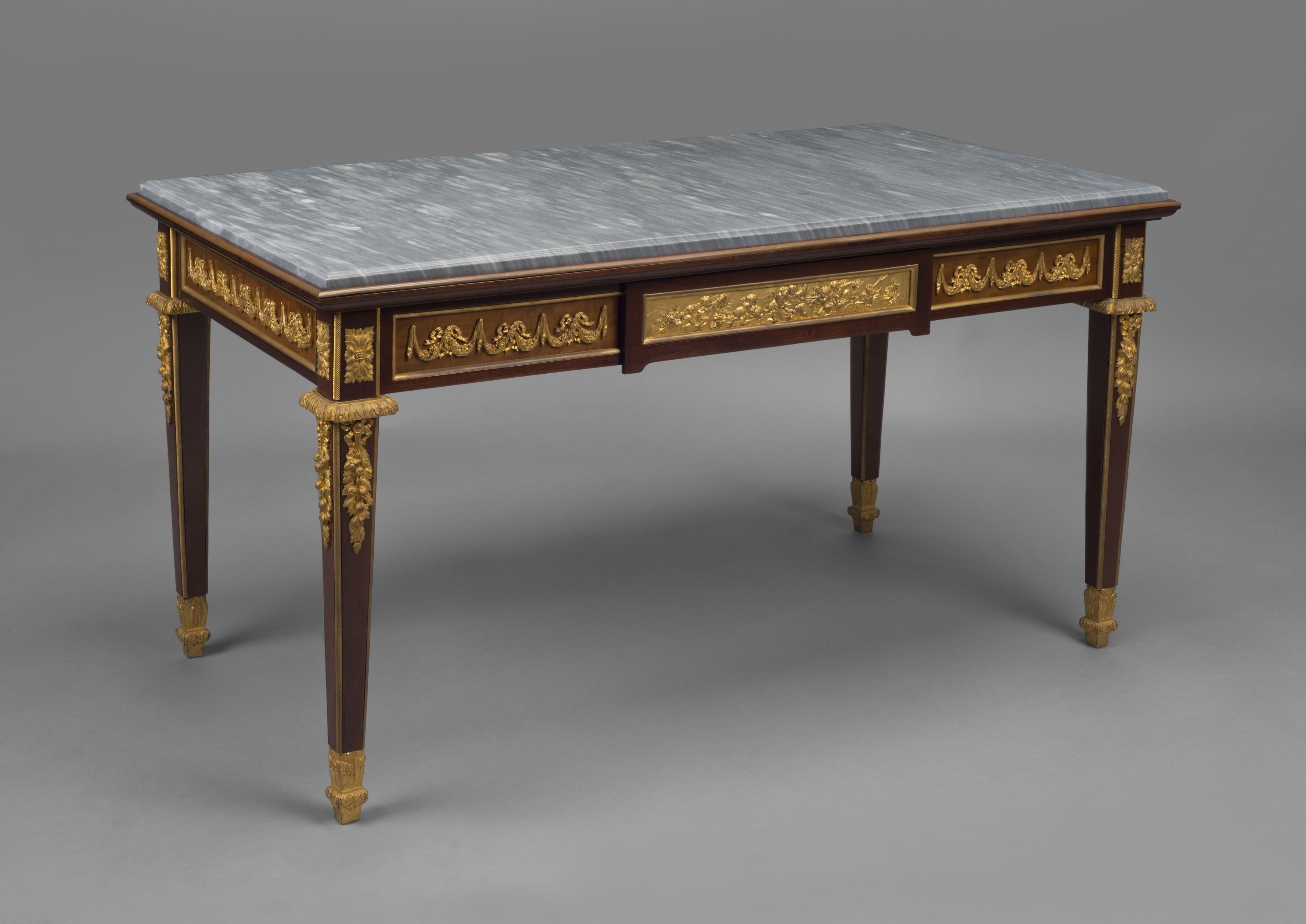 A Louis XVI Style gilt bronze mounted mahogany low table with a grey marble top.

French, circa 1890.

This table has a rectangular grey marble top above a frieze with a central drawer with a Fine gilt bronze plaque depicting putti at play,