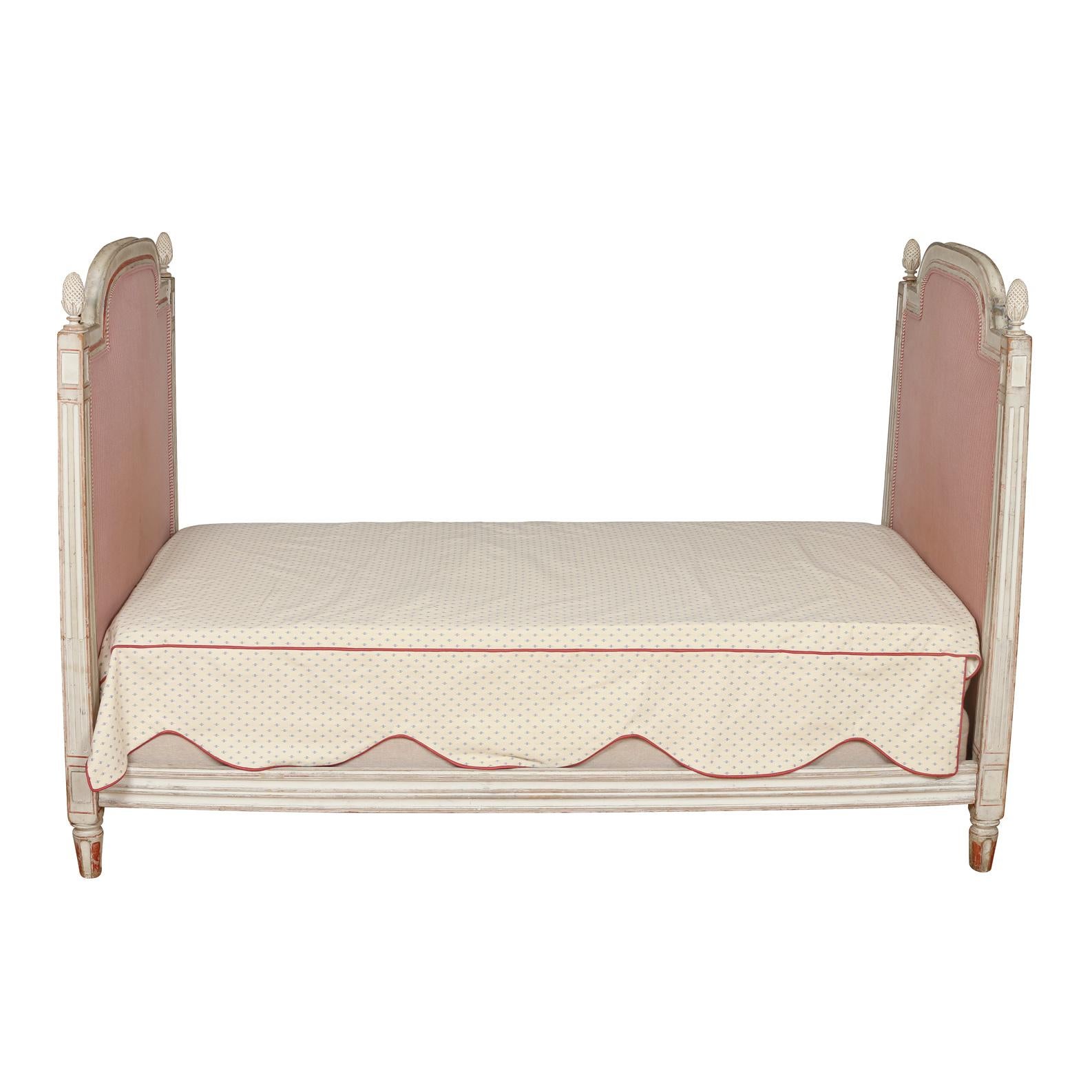 A charming painted daybed in the Louis XVI style, this gem could be the centerpiece of a room. Made up of two ends upholstered in a pink/red ticking stripe, this piece features a grayish white finish with red trim and features lovely carved details,