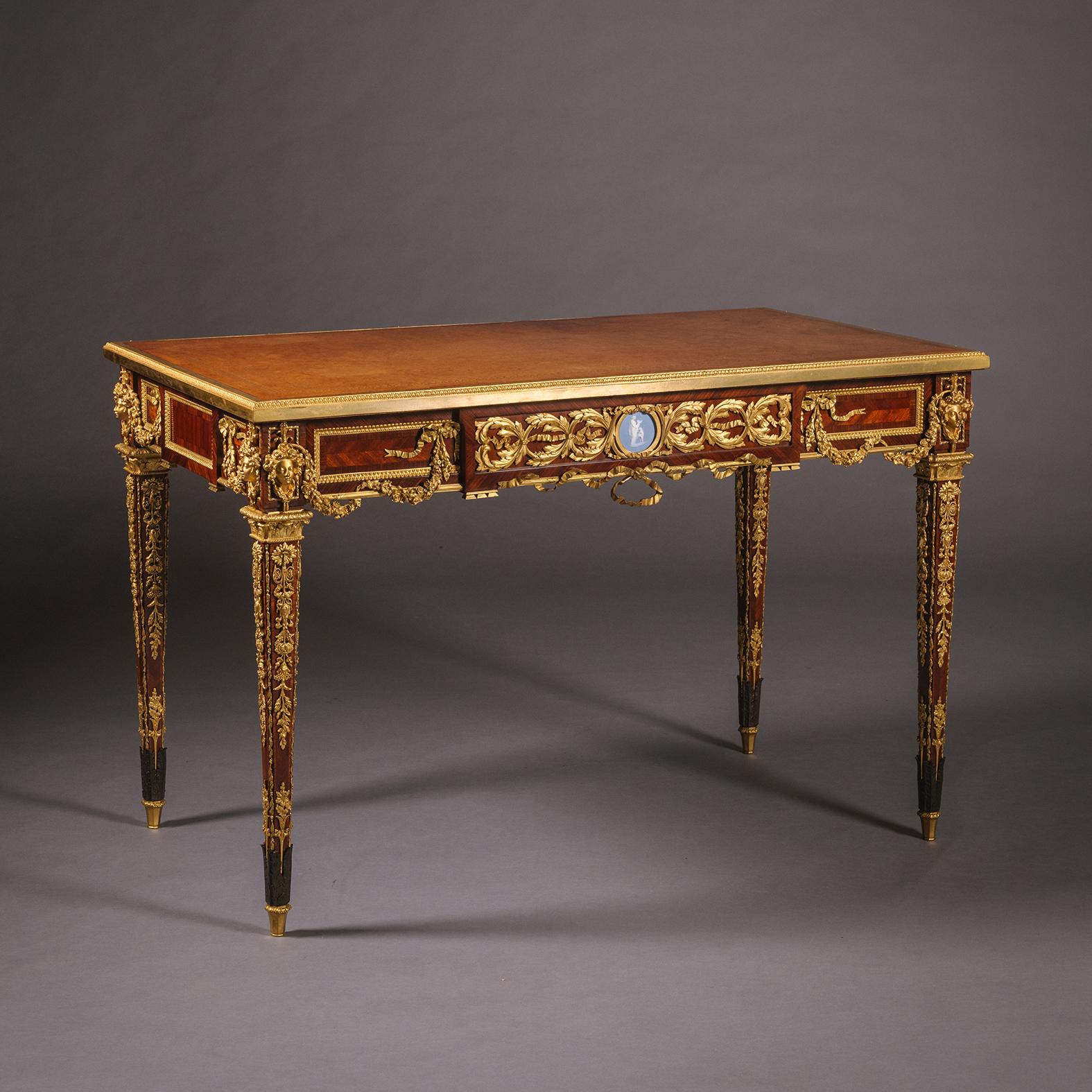 A Louis XVI Style Gilt-Bronze Mounted Bois Satiné Parquetry Inlaid Writing Table, By Emmanuel Zwiener, Paris.

The top of gilt-tooled tan leather surrounded by a stiff-leaf cast edge. The frieze drawer centred by a fine neo-classical Jasperware