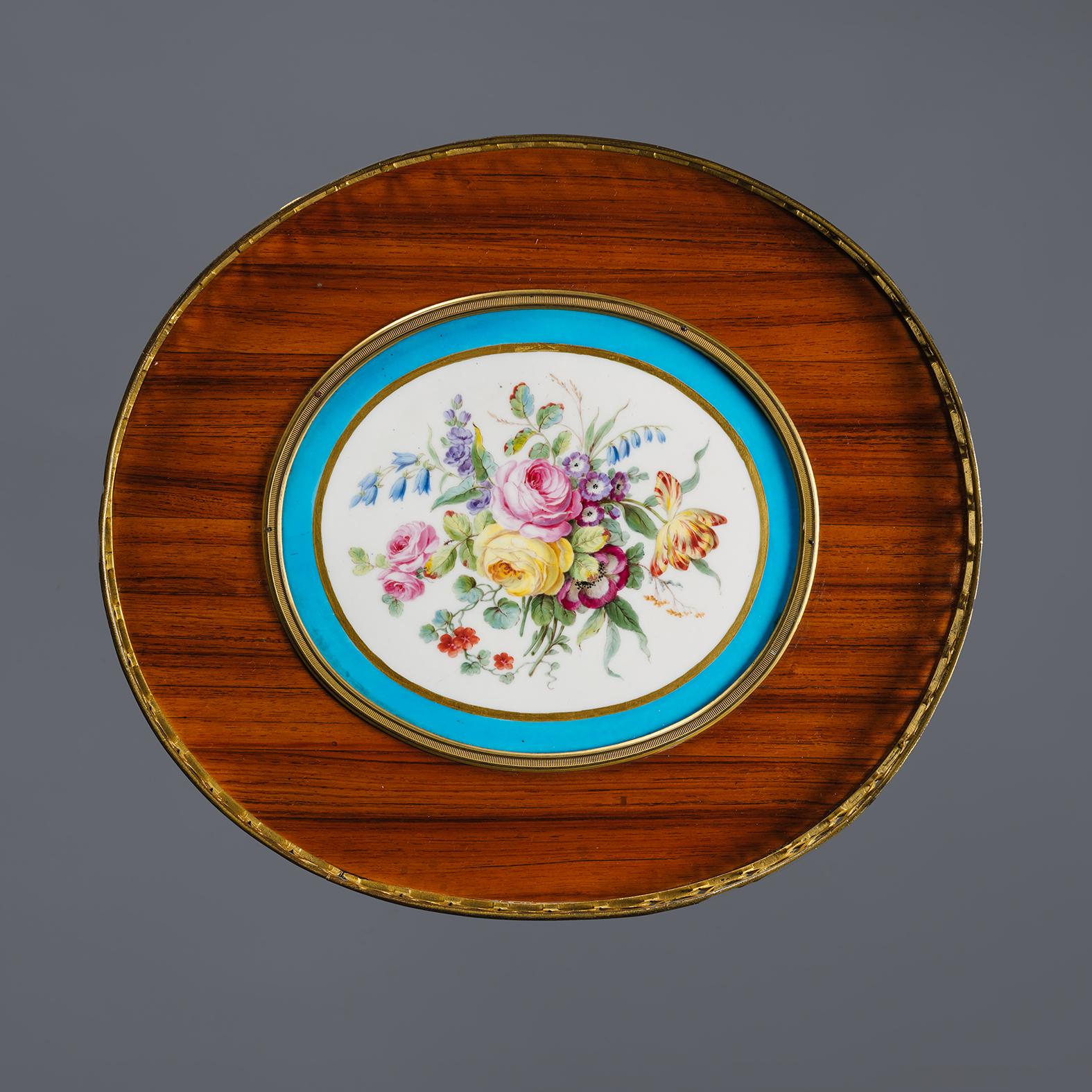 A Louis XVI Style Porcelain Mounted Gueridon.

The oval top with a pierced gallery centred by an inset Sèvres-style porcelain plaque painted with a floral bouquet, raised on tapering legs united by a galleried undertier.  

French, Circa 1850.