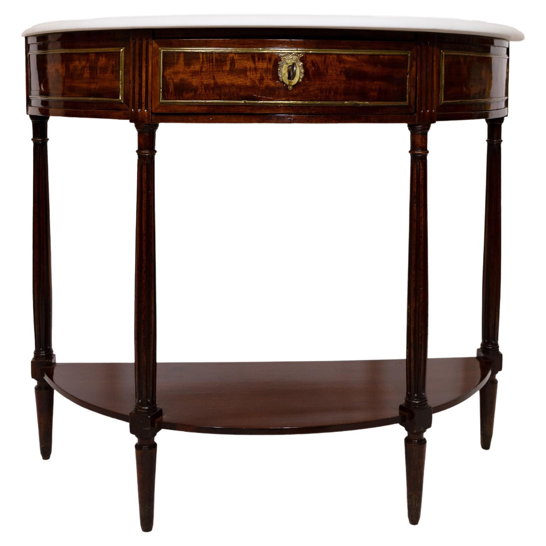 A French Louis XVI-style small scale demilune console table with drawer and apron and four round tapered legs with stretcher in form of lower shelf. The apron with figured mahogany veneer with brass molded edge detail and a keyhole with escuchen.
