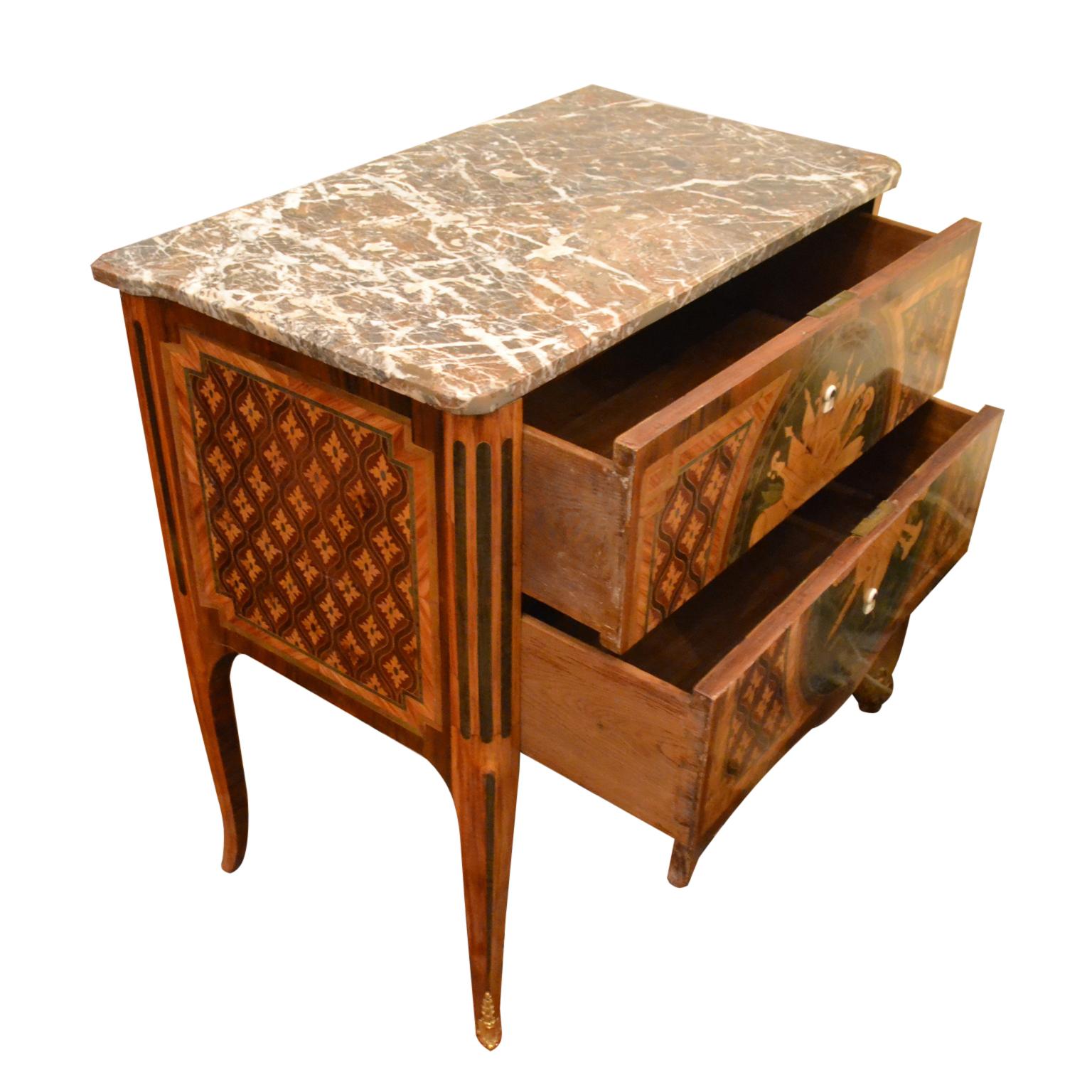 A period 18th century French two drawer chest with a breche marble top, the oak carcass veneered in various exotic woods in an overall geometric design. The large inlaid oval panel to the front shows various musical instruments in a heraldic