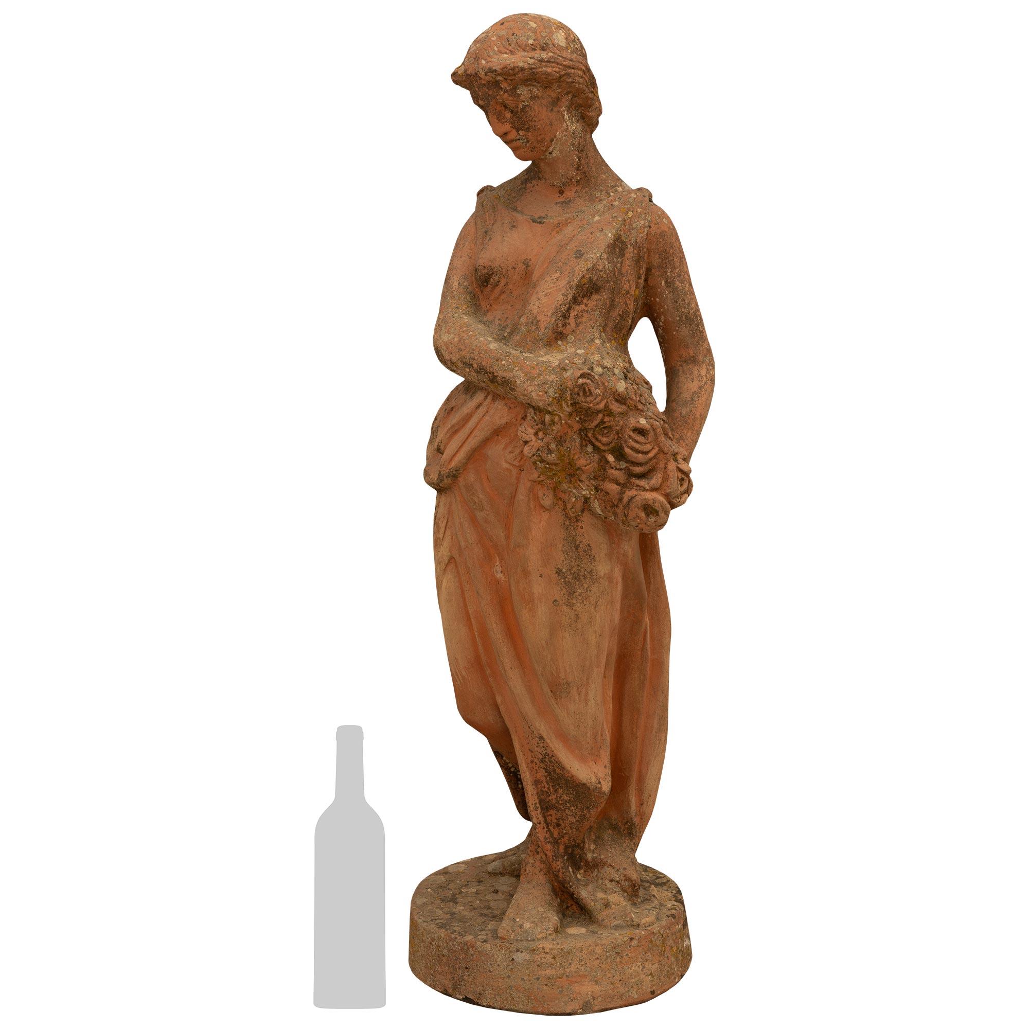 Un'incantevole e unica statua continentale neoclassica della metà del XIX secolo. Statua in terracotta. La bella statua di una fanciulla è vestita con un abito classico e tiene un bouquet di fiori sul lato sinistro. La statua è sostenuta da una base