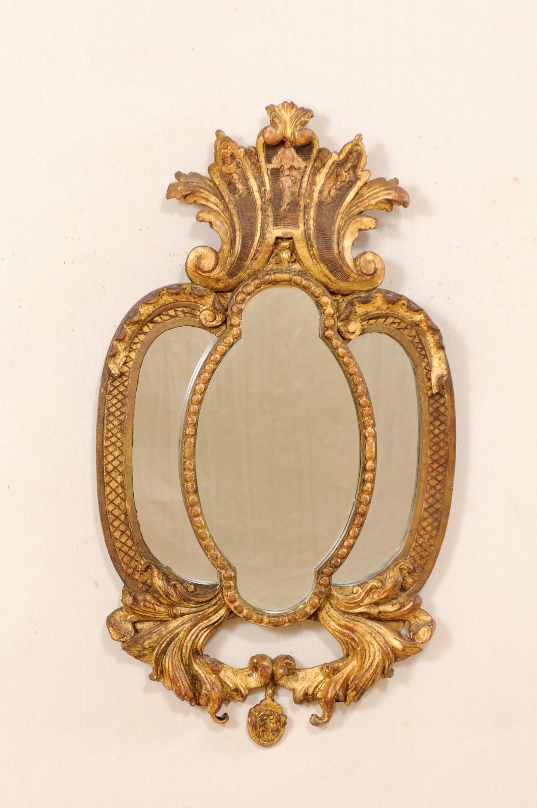 An Italian gilt and carved wood mirror from the early to mid-20th century. This gold-tone mirror from Italy features a beautifully carved surround with an exaggerated crest and bottom in an acanthus leaf motif. The mirror is divided into three