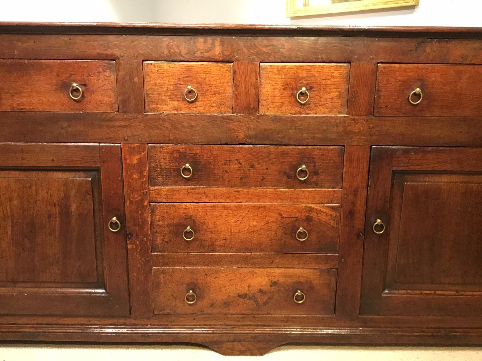 A lovely oak mid-18th century antique dresser base of fabulous color and patination. Having a three plank oak top above an arrangement of seven rectangular oak lined drawers retaining their original brass ring handles with two panelled cupboard