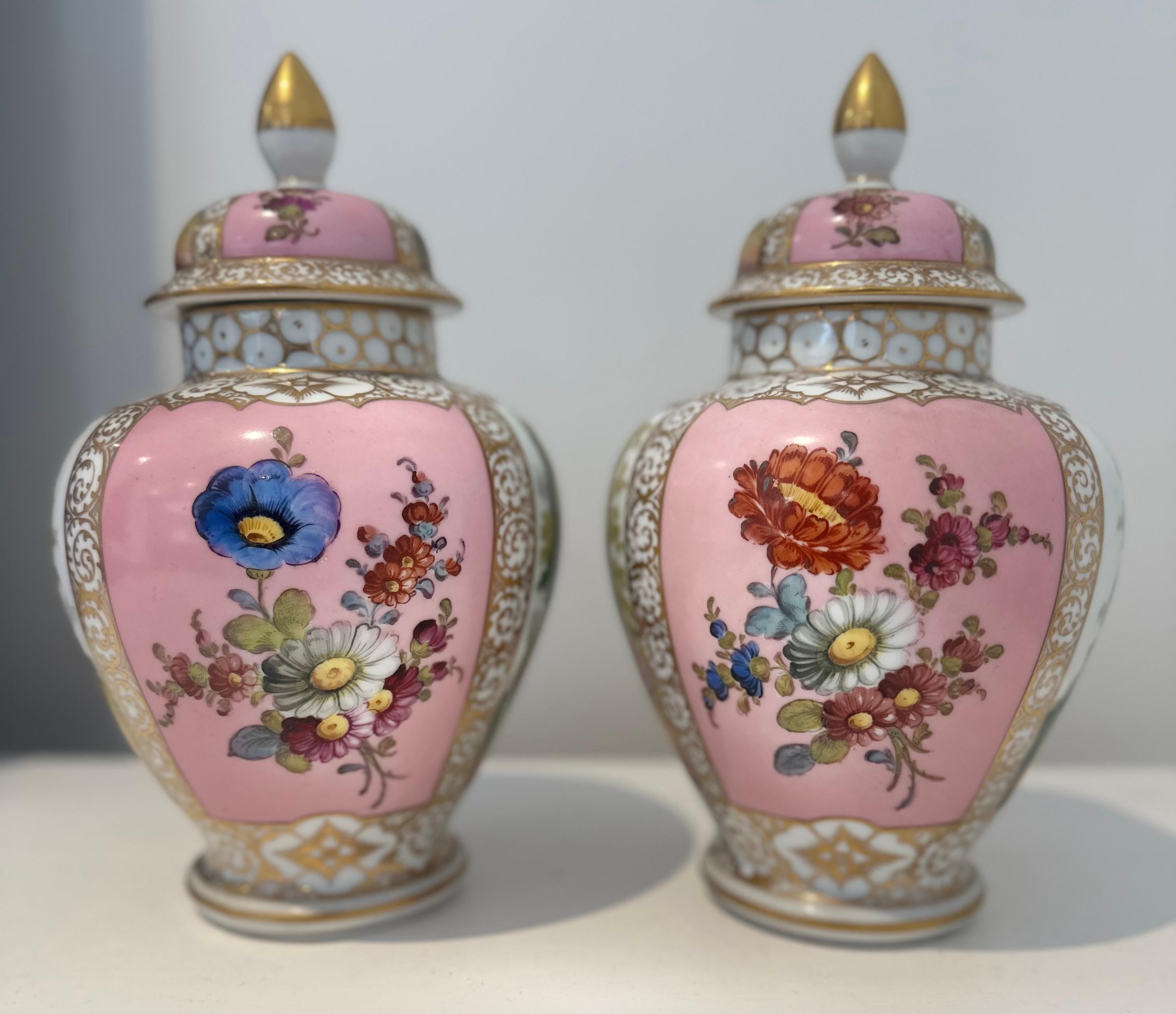 A lovely pair of hand painted porcelain urns with lidded tops . Reflecting scenes of ladies and gentlemen surrounded by flowers and foliage. 