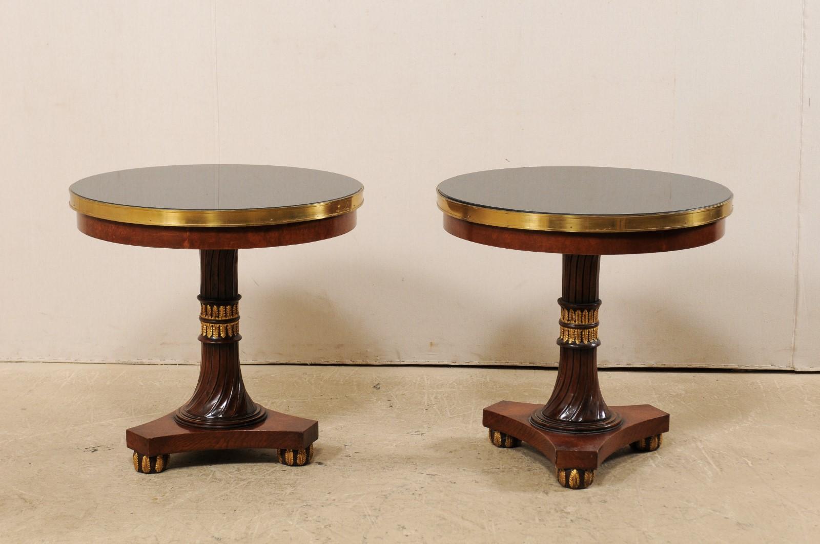 A pair of Italian regency-style, granite top side tables by designer Francisco Molon. This vintage pair of pedestal tables from Italy each feature a round-shaped black granite top, with thick brass banding along perimeter sides, which rests upon a