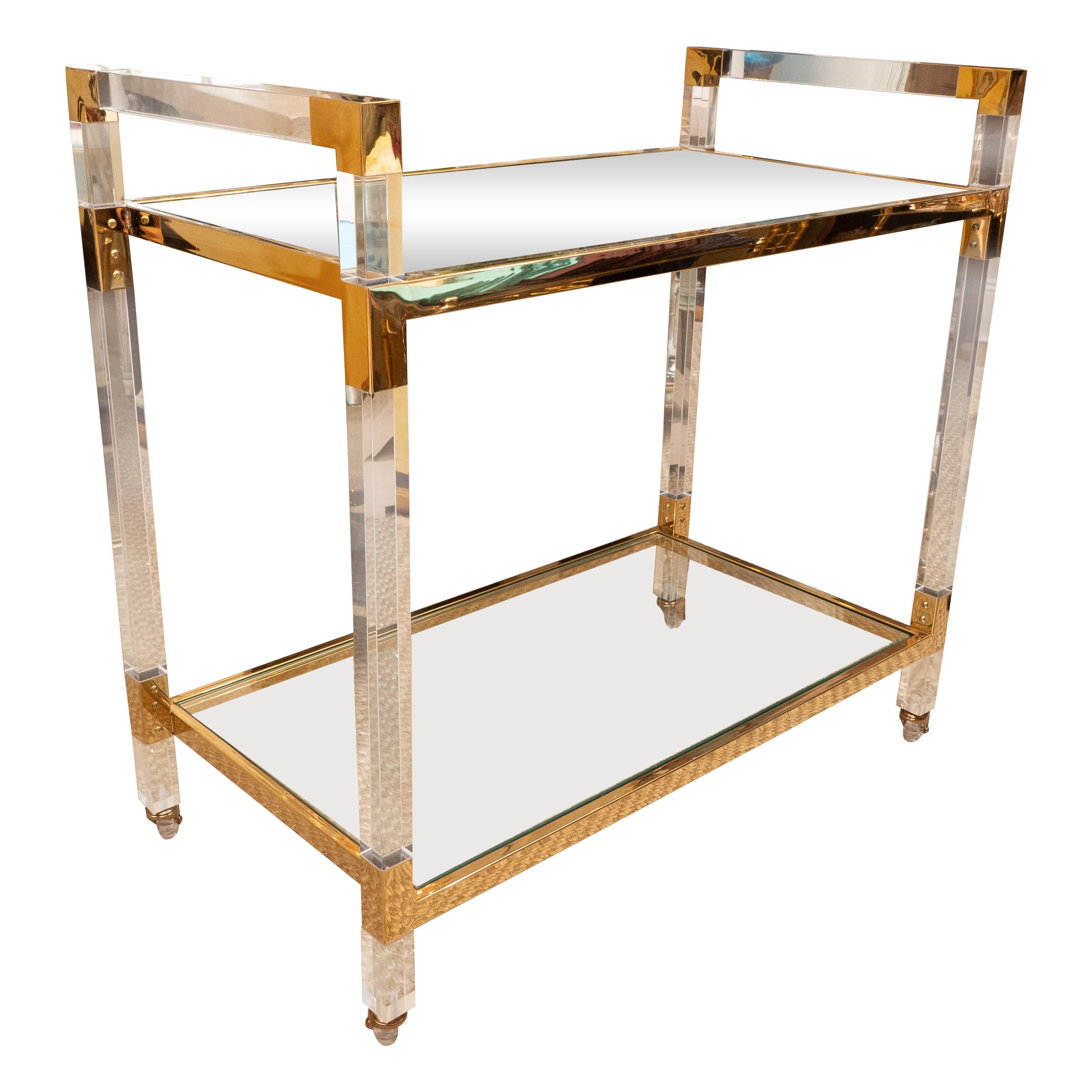 This über chic bar cart will add instant style and glamour to a room. The Lucite frame is accented in brass and holds two glass shelves. The piece sits on castors for easy movement. Despite its light and 