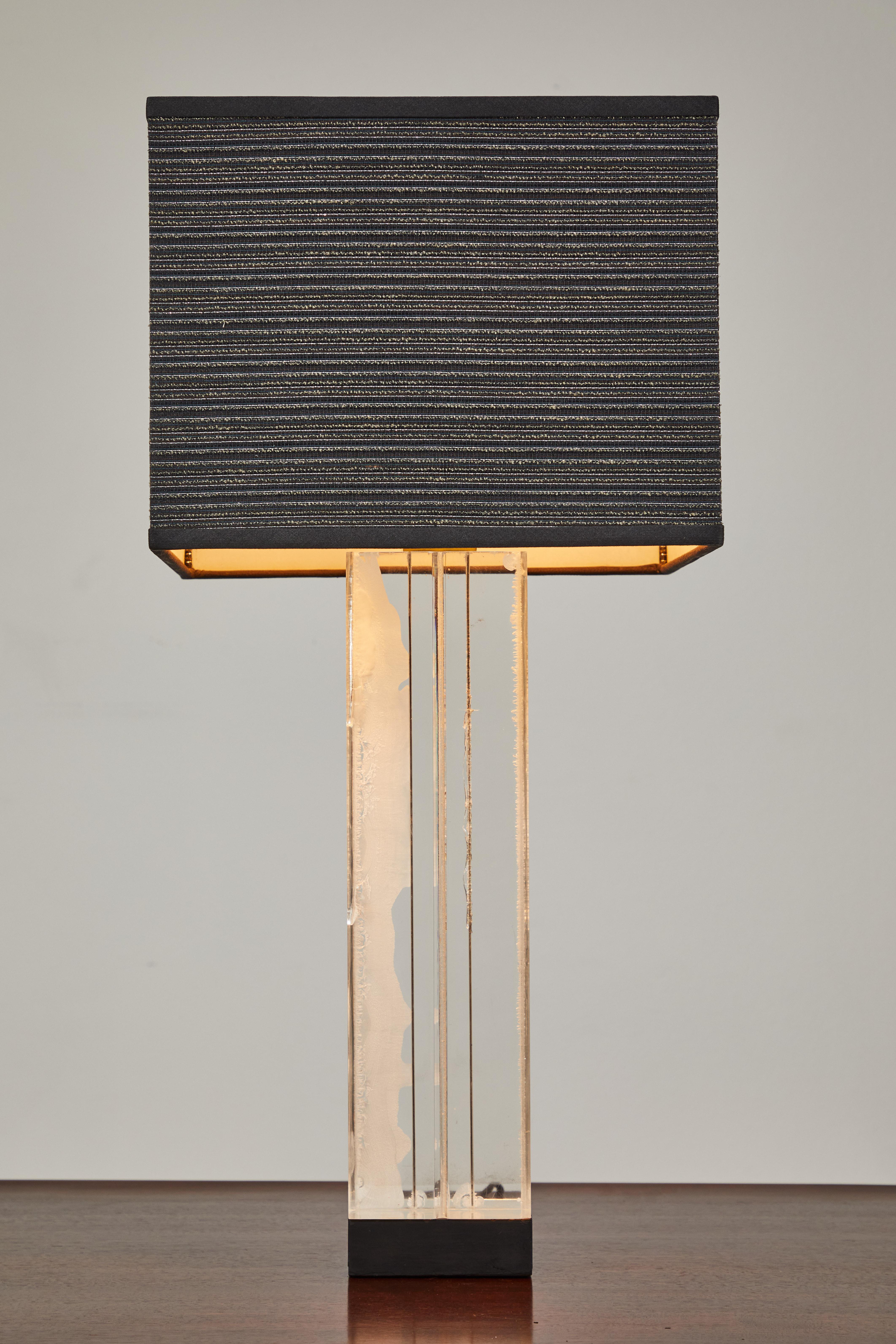 Cette lampe de table Billy Haines présente un bloc proéminent de lucite biseautée de 17,5 po de haut sur 5 po de large. La base est en bois et peinte en noir. Le nouvel abat-jour personnalisé est une soie noire recouverte d'un tissu à battants en