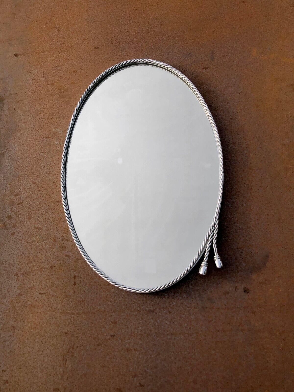 An elegant and luxurious oval wall mirror, Art-Deco, Neo-Classical, with a frame decorated with intertwined metal rope, decorated with a double trimmings on the lower right side, in bronze or silver-plated brass, in the spirit of Maria Pergay, by