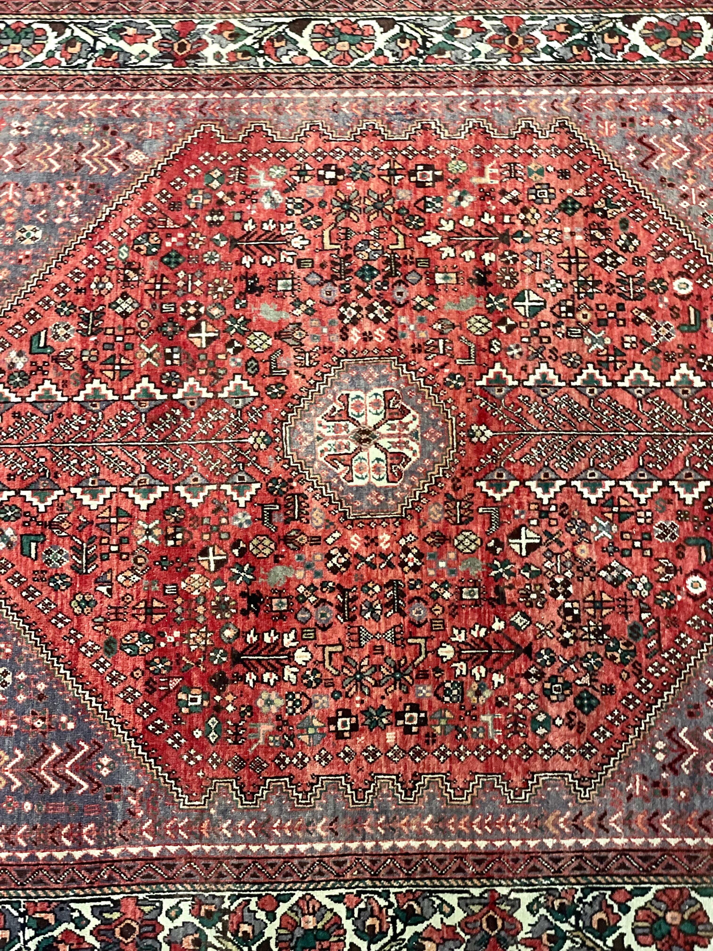 A luxurious antique Persian rug, in a medallion design woven in vivid tones of red and cream. A central diamond-shaped field contains geometric and stylised designs, while the spandrels, in more subdued hues, are accented with octagonal cream
