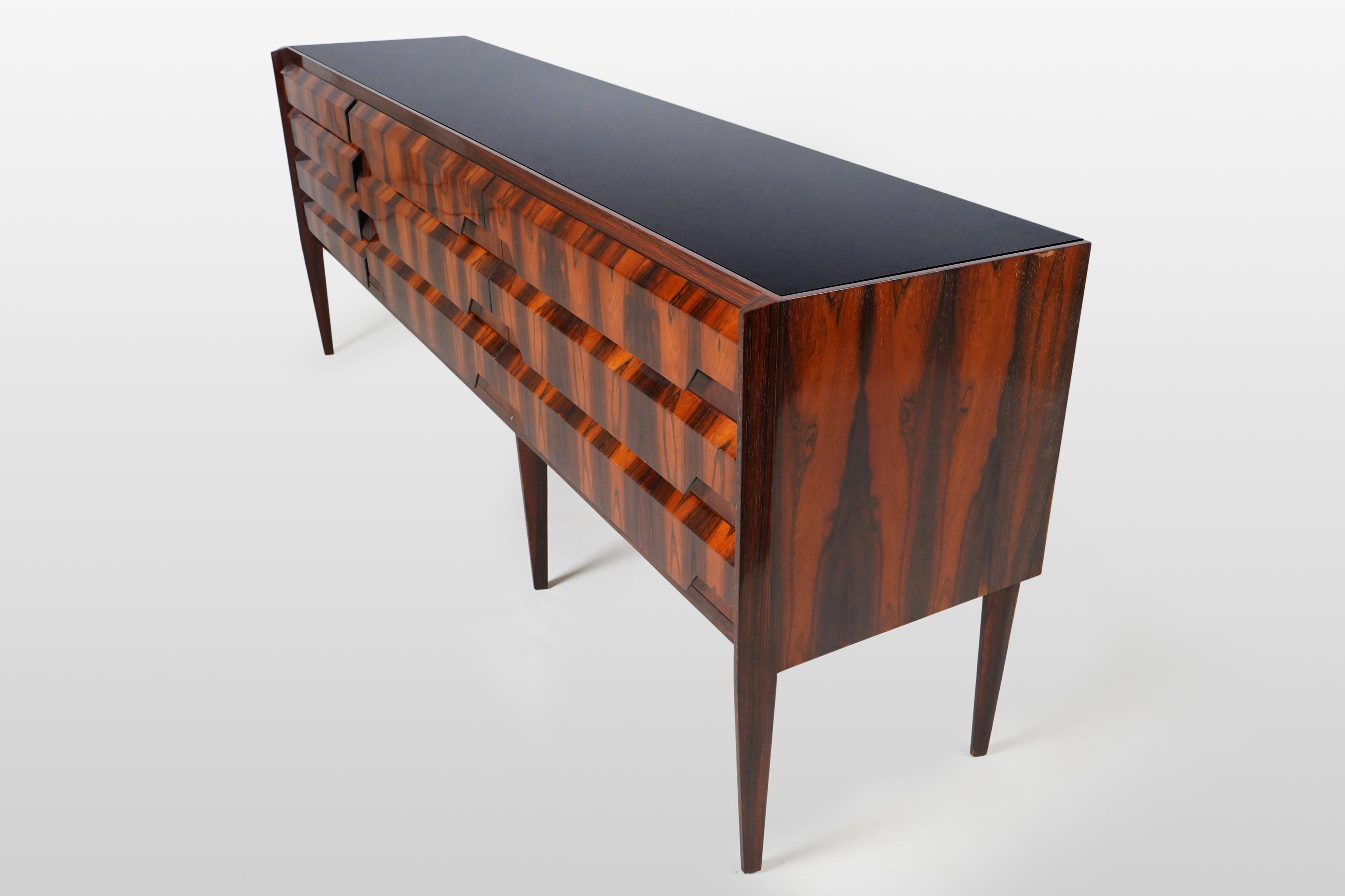 This exceptional sideboard features richly figured Makassar veneers, a black glass top and ten drawers. It's quite rare to see veneer applied vertically to relatively shallow drawers and the effect is very dramatic. The chamfered drawer fronts with