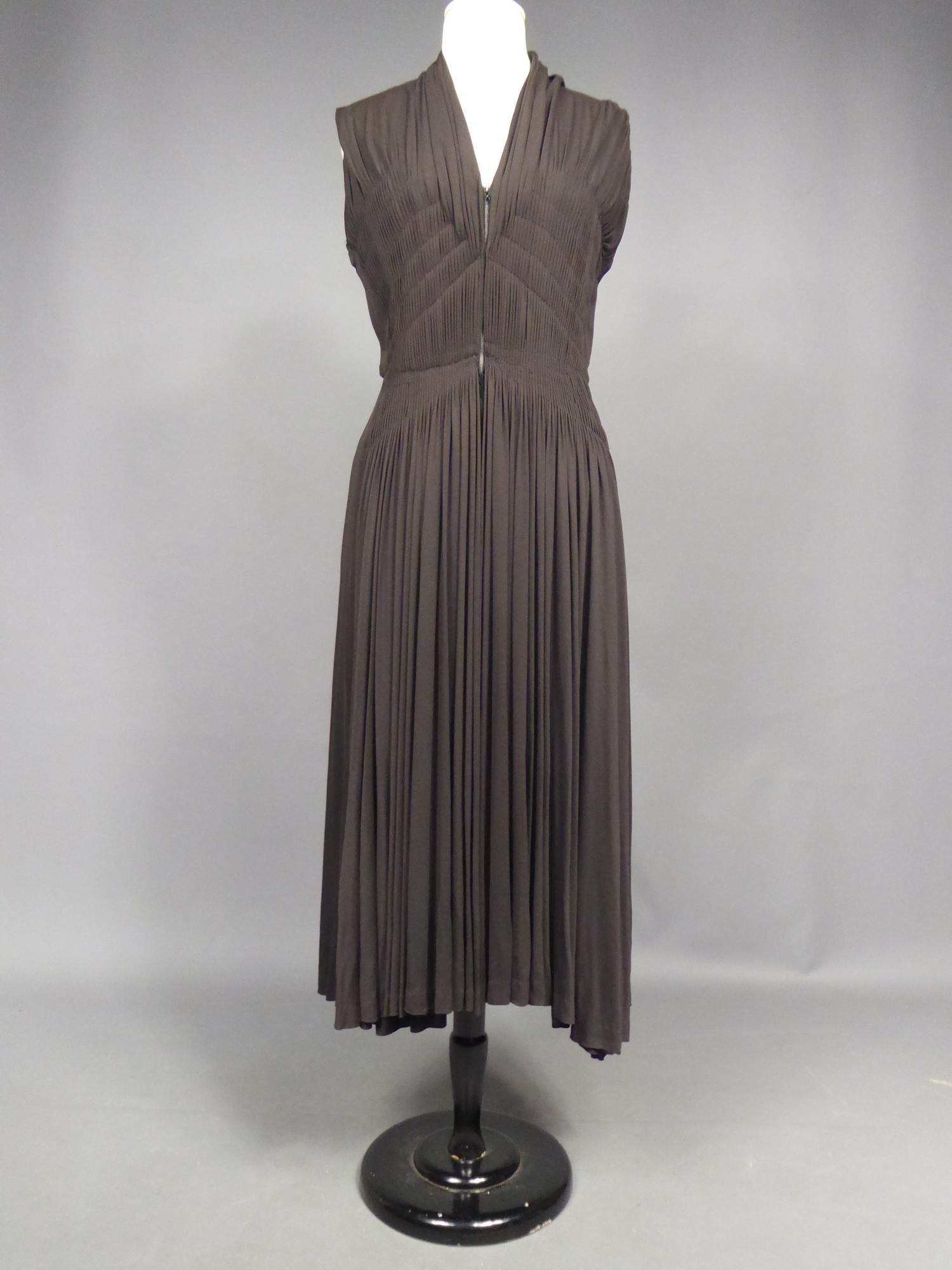 Circa 1950

France

Superbe robe de cocktail attribuée à Madame Grès en jersey de soie brun foncé à bolduc numérotée 63926 datant de la fin des années 1940. Robe sans manches à l'encolure pointue et au jersey plissé ruché:: dessinant en diagonale la