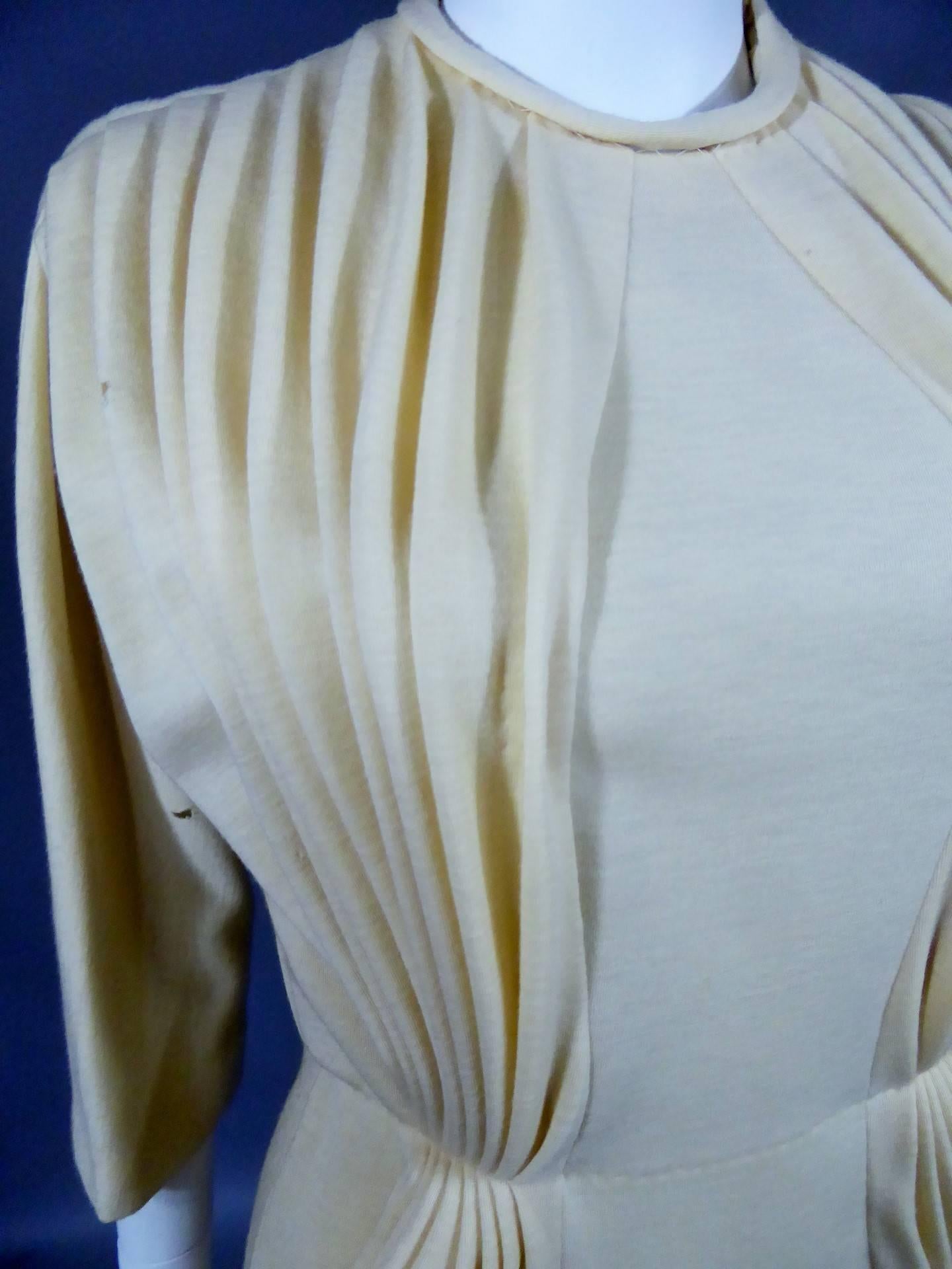 Circa 1970
France
 Prototype de robe de parade attribué à Madame Grès et datant des années 1970. Bolduc de coton blanc cousu indiquant le n° 144 à Christine Vicky. Jersey de laine beige, non doublé. Le travail de plissage accentue les poches sur les