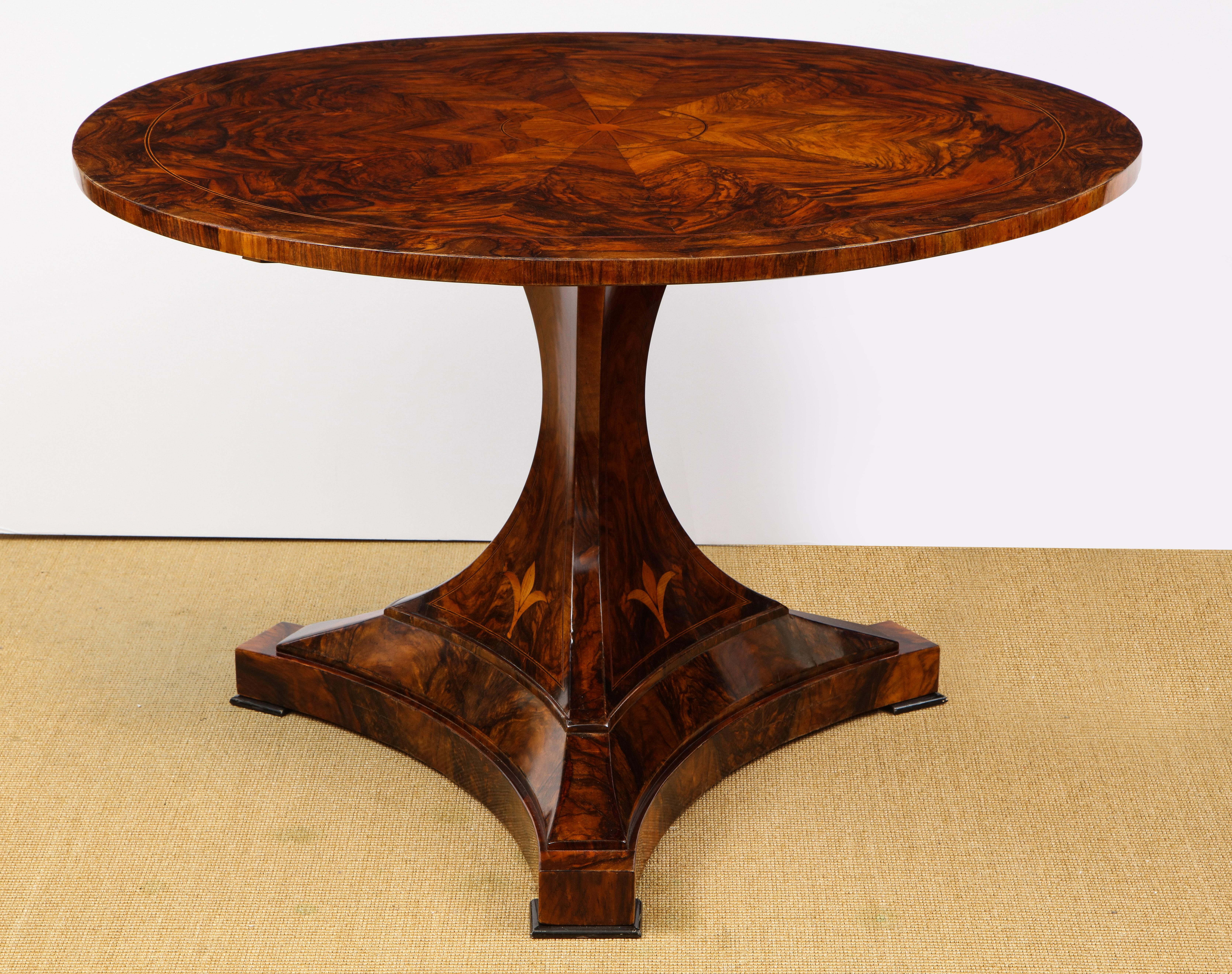 The bookmatched burl walnut veneered top with fruit inlay over a similarly veneered tripart pedestal and stepped base.
 