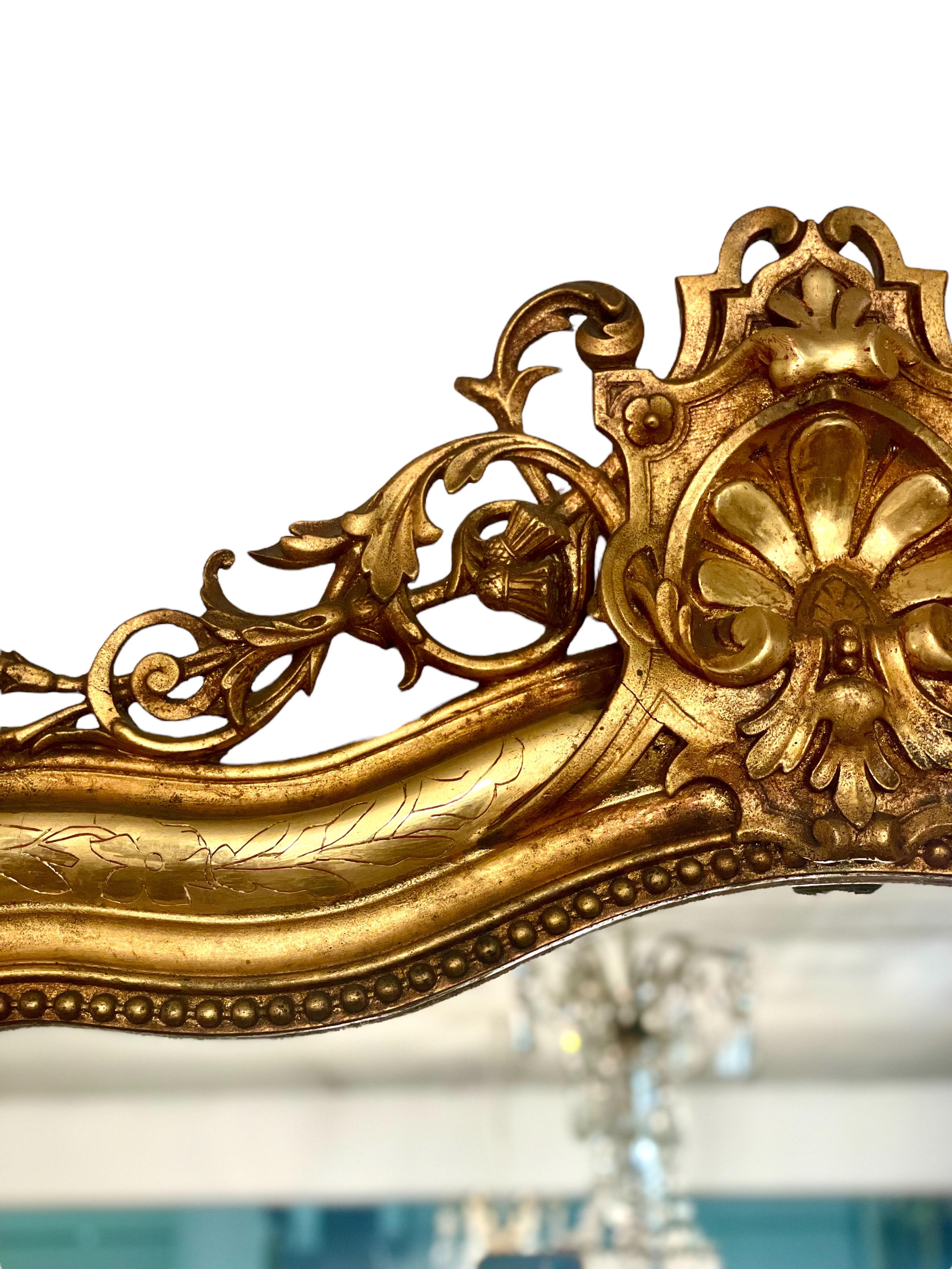 A magnificent late 19th century Louis XV style gilt overmantel mirror, in wood and gilded stucco, with string-of-pearls beading to the interior perimeter, and a tumbling openwork cartouche. This beautiful mirror features a wonderfully sleek, fluted
