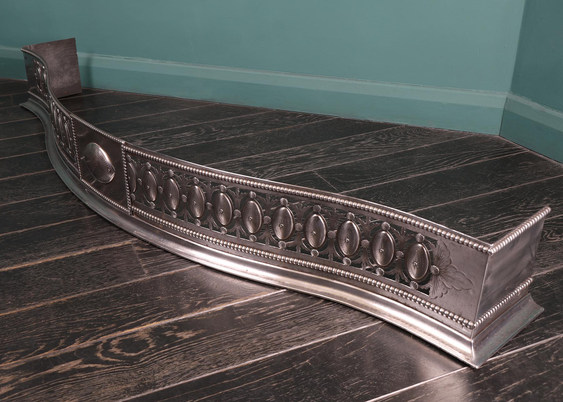 A magnificent polished steel Regency serpentine fireplace fender, the central rectangular tablet with incised circular patera. The surrounding frieze with pierced and engraved oval patera enclosed with harebells all set between beaded mouldings. The