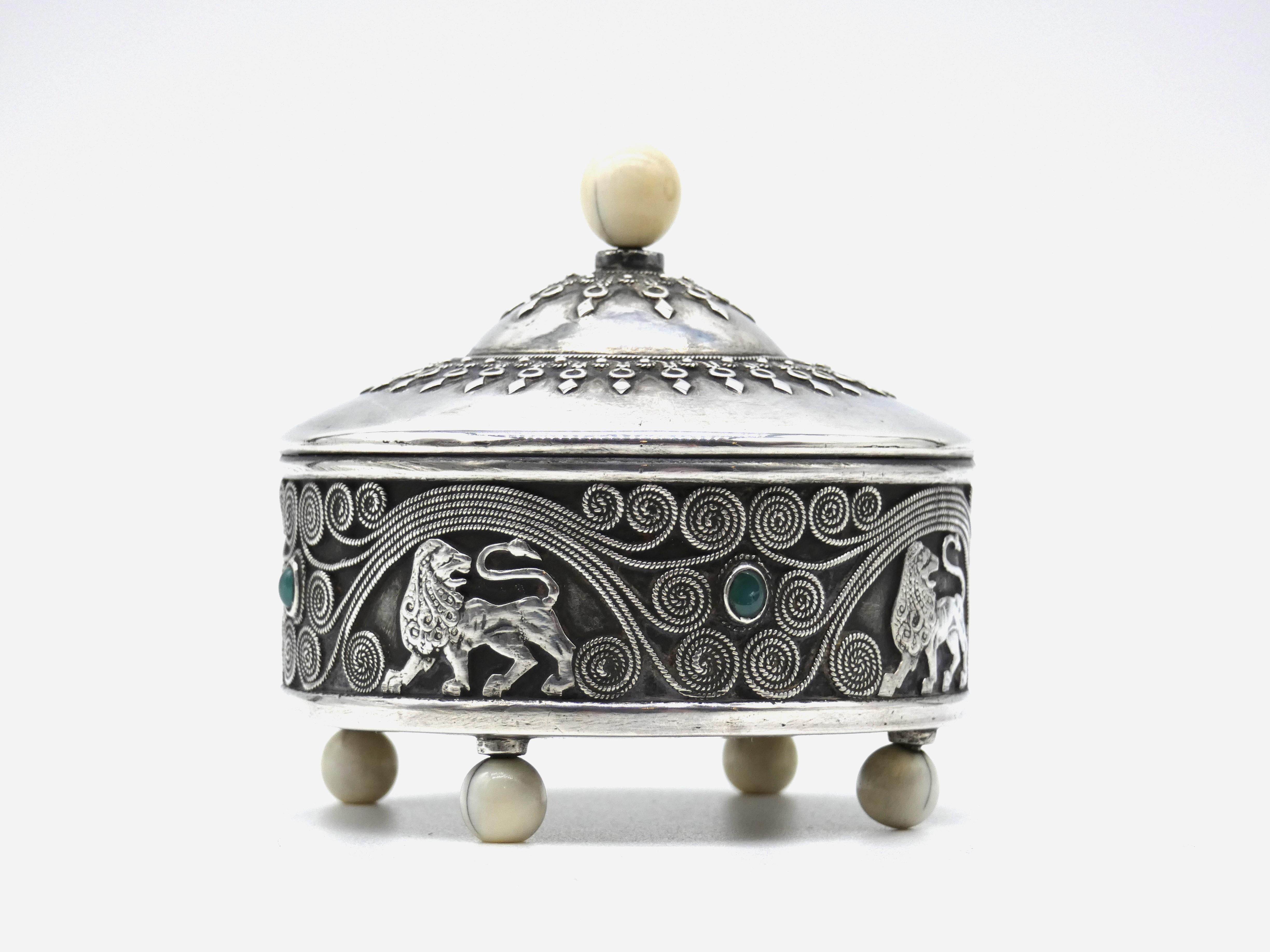Spice container stands on four ball shaped ivory feet attached to base. Container is decorated with detailed filigree lions, scrolling designs and embellished with four emerald colored gemstones. Removable cover is stylishly chased with diamond