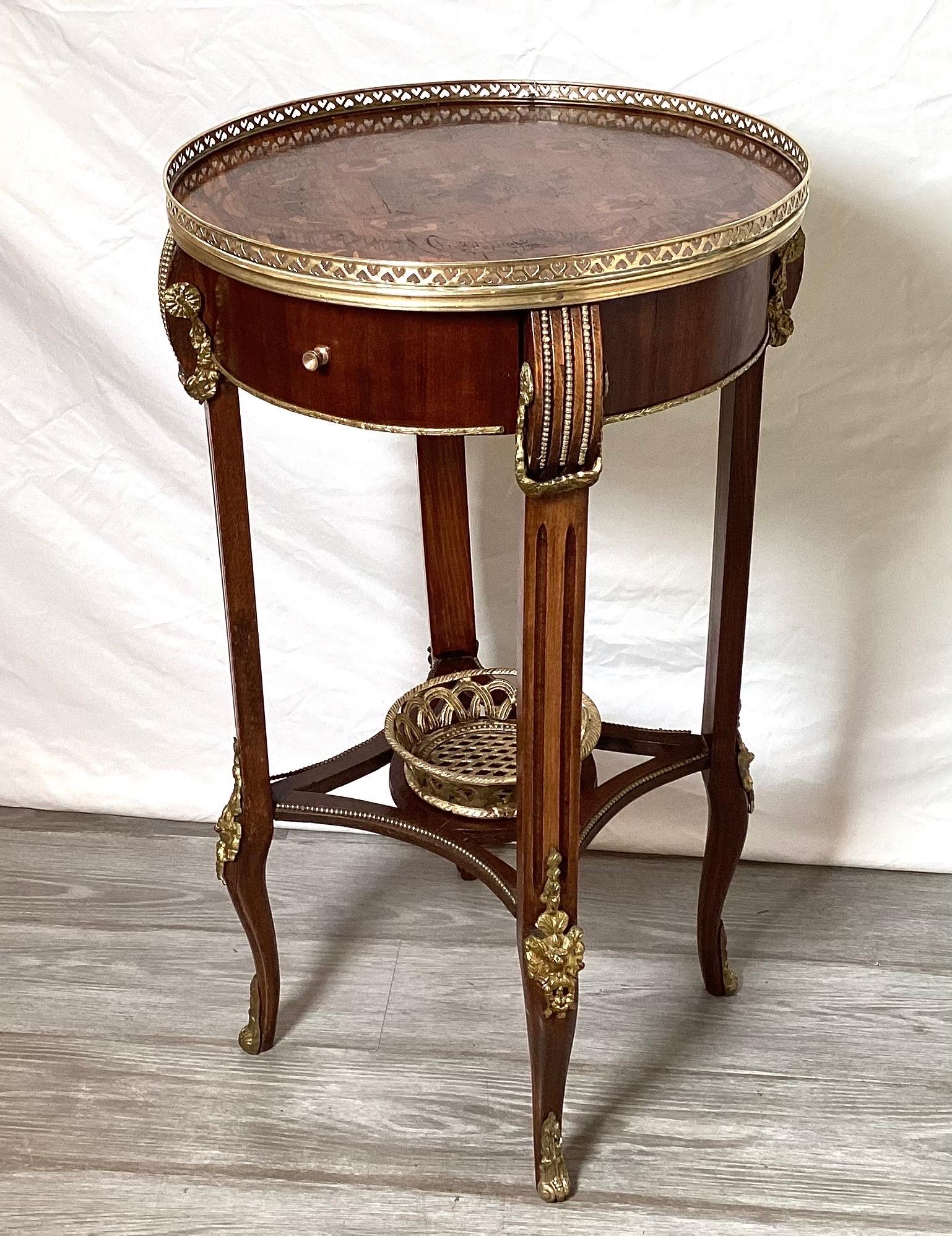 An elegant round accent side table in the Louis XV style. The mahogany and tulipwood inlaid top with pierced gallery edge with shapely legs with attached gilt mounts. The stretcher base with a pierced git bronze basket attached. The table is