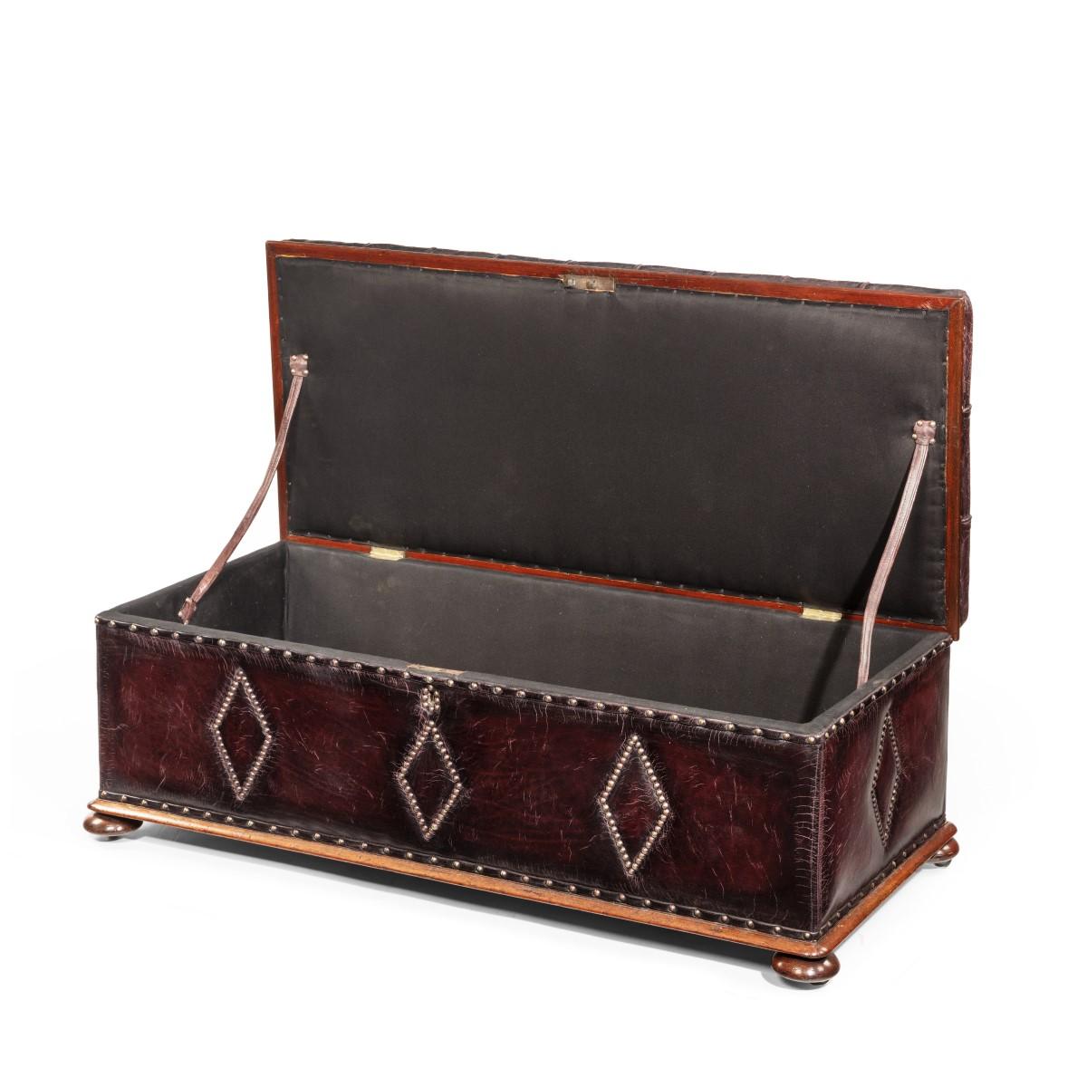 A mahogany box ottoman, of long rectangular form with a hinged lid and tapering sides, re-upholstered in burgundy leather, the top deep-buttoned and the sides with close-nailed brass lozenges, set on bun feet. English, circa 1860.

  