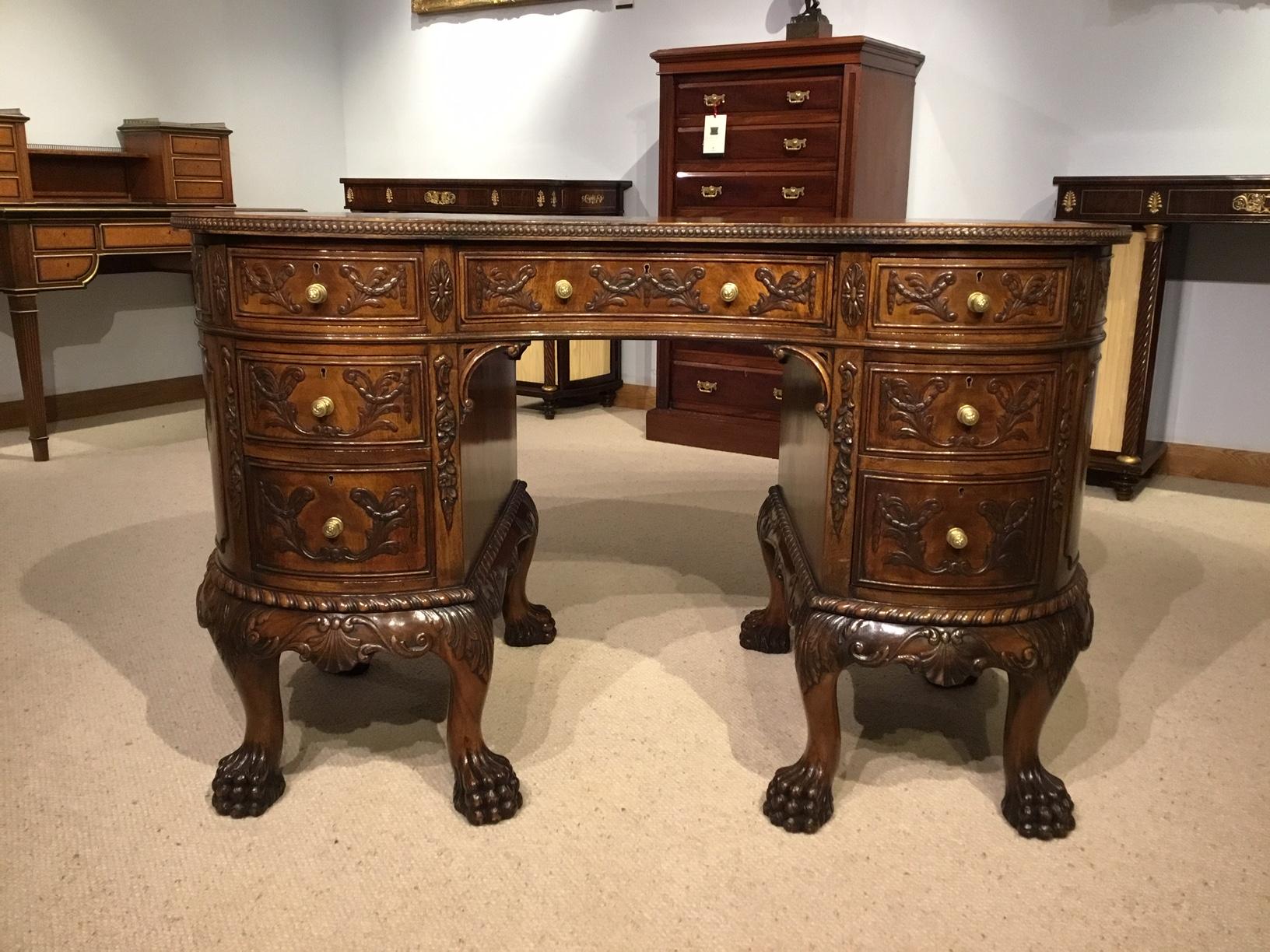 A mahogany Chippendale Revival kidney shaped writing desk. Having a kidney shaped top with the original faded tan leather writing surface with flame mahogany banding. The front has an arrangement of seven mahogany lined drawers with finely carved