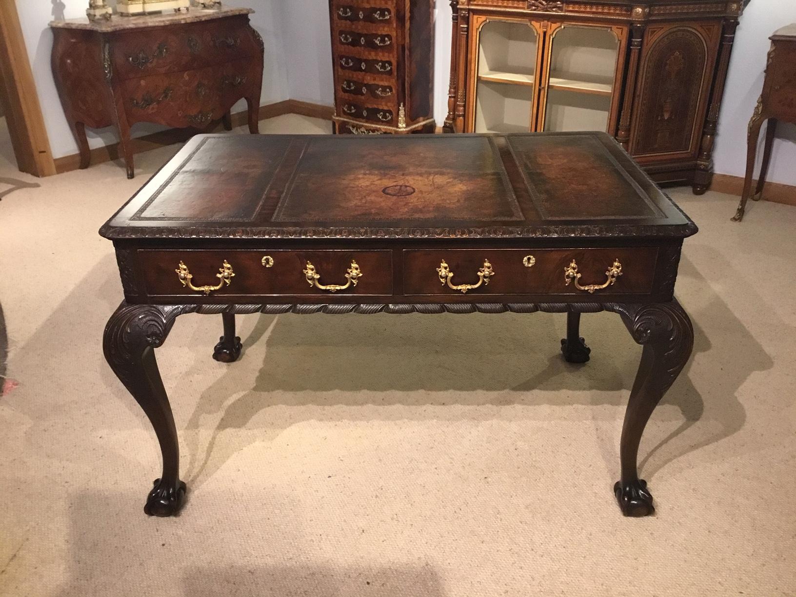 A mahogany Chippendale Revival writing table by Maple & Co of London. Having a rectangular top with three brown leather writing inserts with blind tooled detail and cross banded in flame mahogany with finely carved moulding. The front with two flame