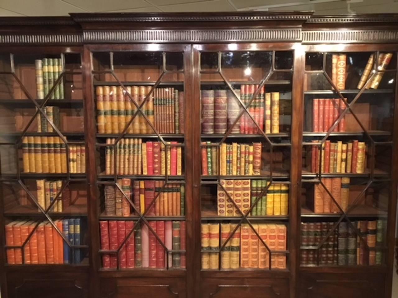 A mahogany George III style breakfront bookcase. The cornice of breakfront outline having dentil moulding and a fluted frieze above an arrangement of four astragal glazed doors enclosing twelve adjustable shelves with flame mahogany panels beneath.