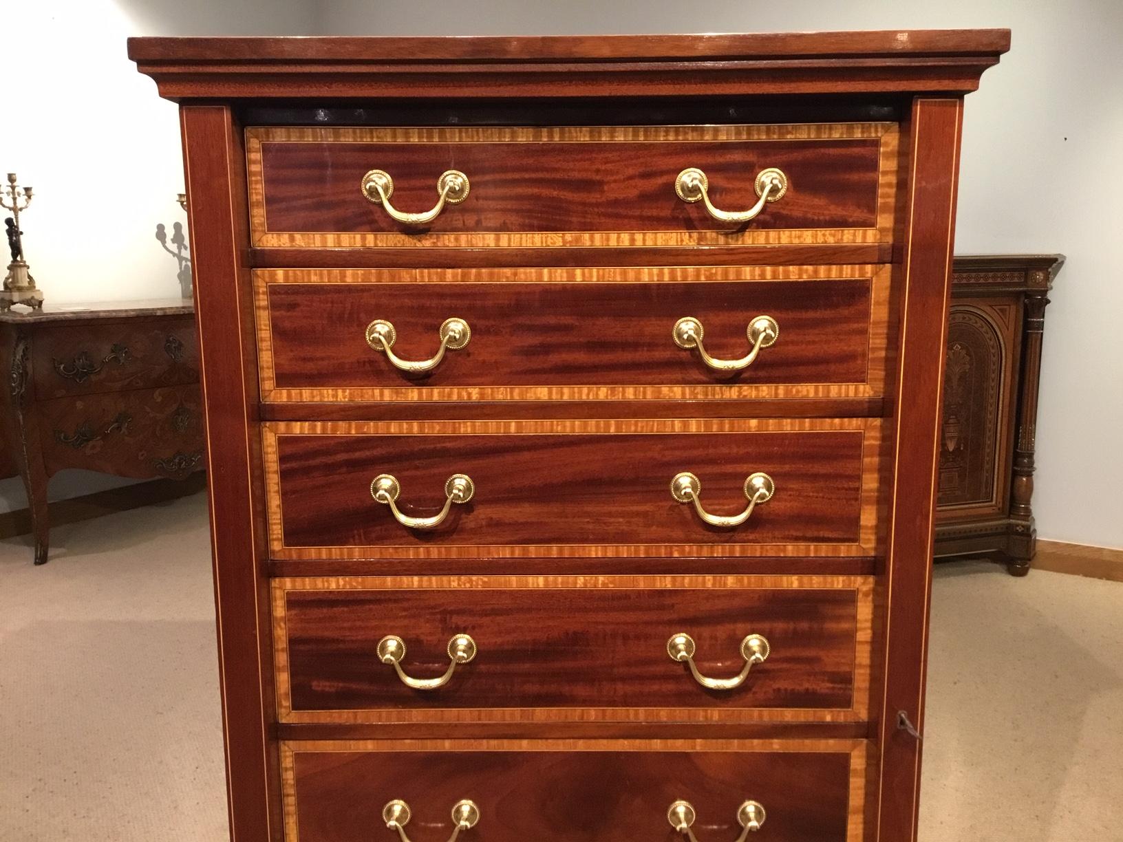 A mahogany inlaid Edwardian period antique wellington chest. Having a solid mahogany rectangular top banded in satinwood with a central shell inlaid paterae, above an arrangement of seven mahogany lined graduating drawers, each with solid mahogany