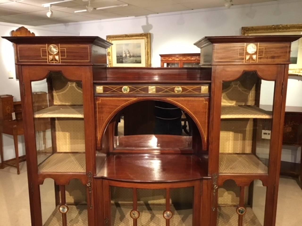 A mahogany inlaid Shapland & Petter display cabinet. With a flared moulded cornice to each end above stylized mother-of-pearl and satinwood inlaid panels with glazed doors beneath, enclosing the original silk lined shelves and back with fine