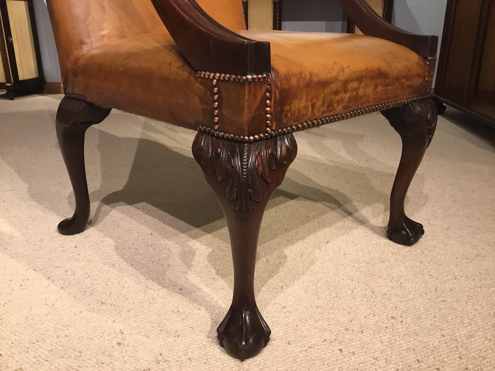 A mahogany and leather George III style Gainsborough armchair. Having a high back, open swept arms and a very generous sprung seat upholstered in a tan leather with brass close studded detail. Having a chamfered mahogany supports to the arms and