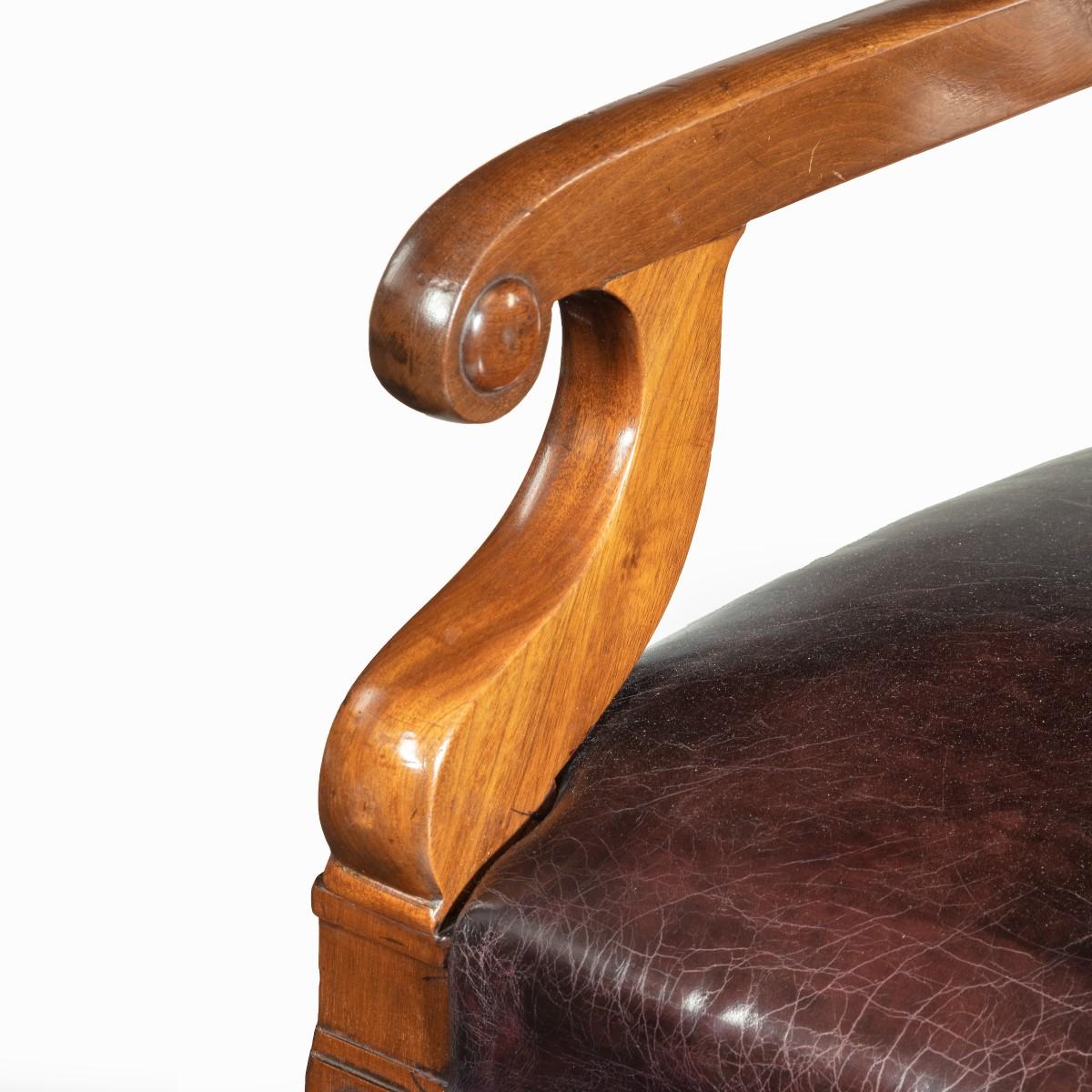 A mahogany library chair in the manner of Henry Holland reputedly made for the United Services Club, the rectangular back with a leather-inset splat and scroll arms, the seat re-upholstered in distressed burgundy leather above turned, tapering front