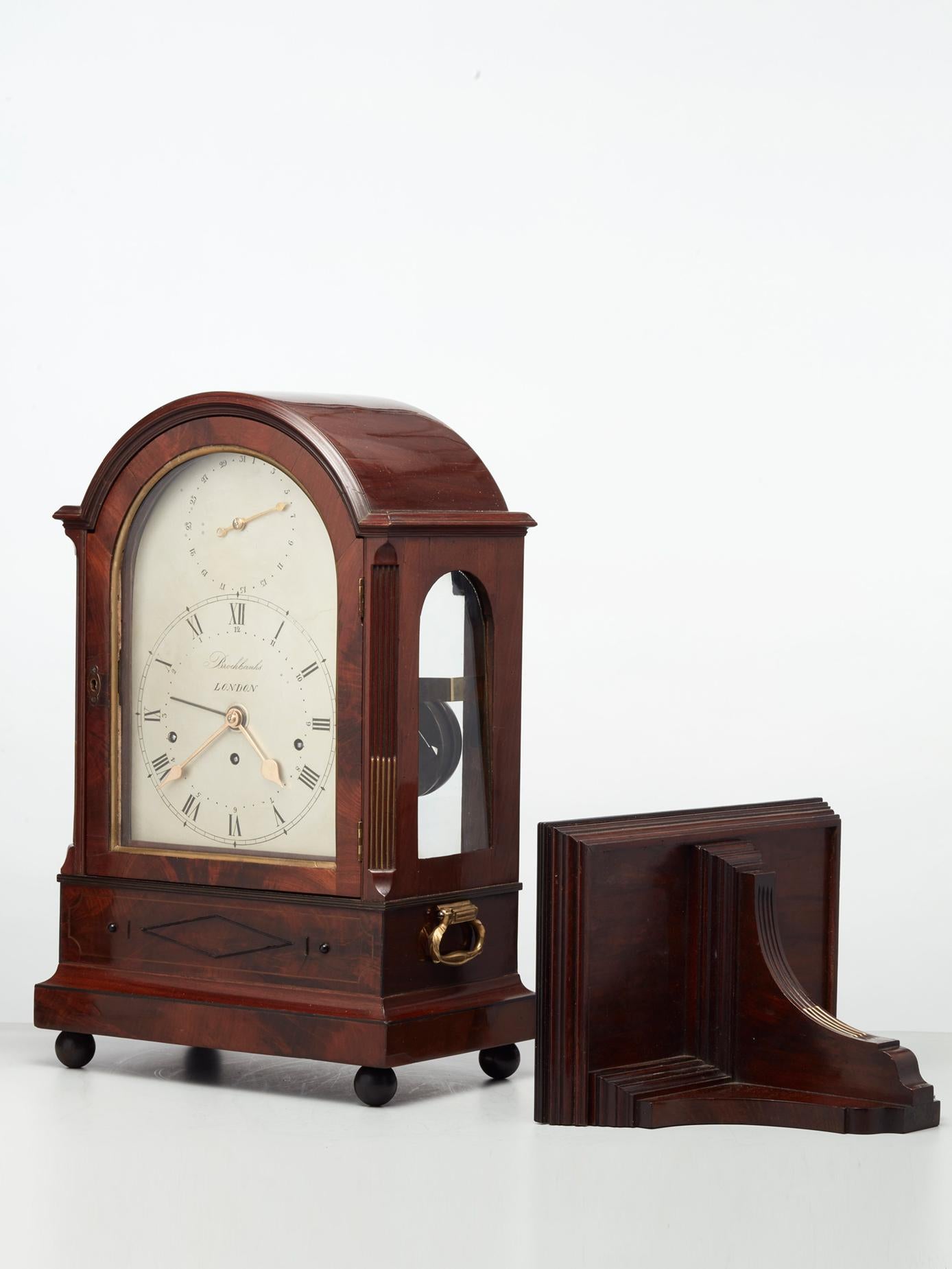 A very different English Regency, mid nineteenth century mahogany bracket clock with matching bracket, circa 1830.

The case with arched top and side arched glass apertures, the corners decorated with brass inlay. Below the dial, lovely ebony