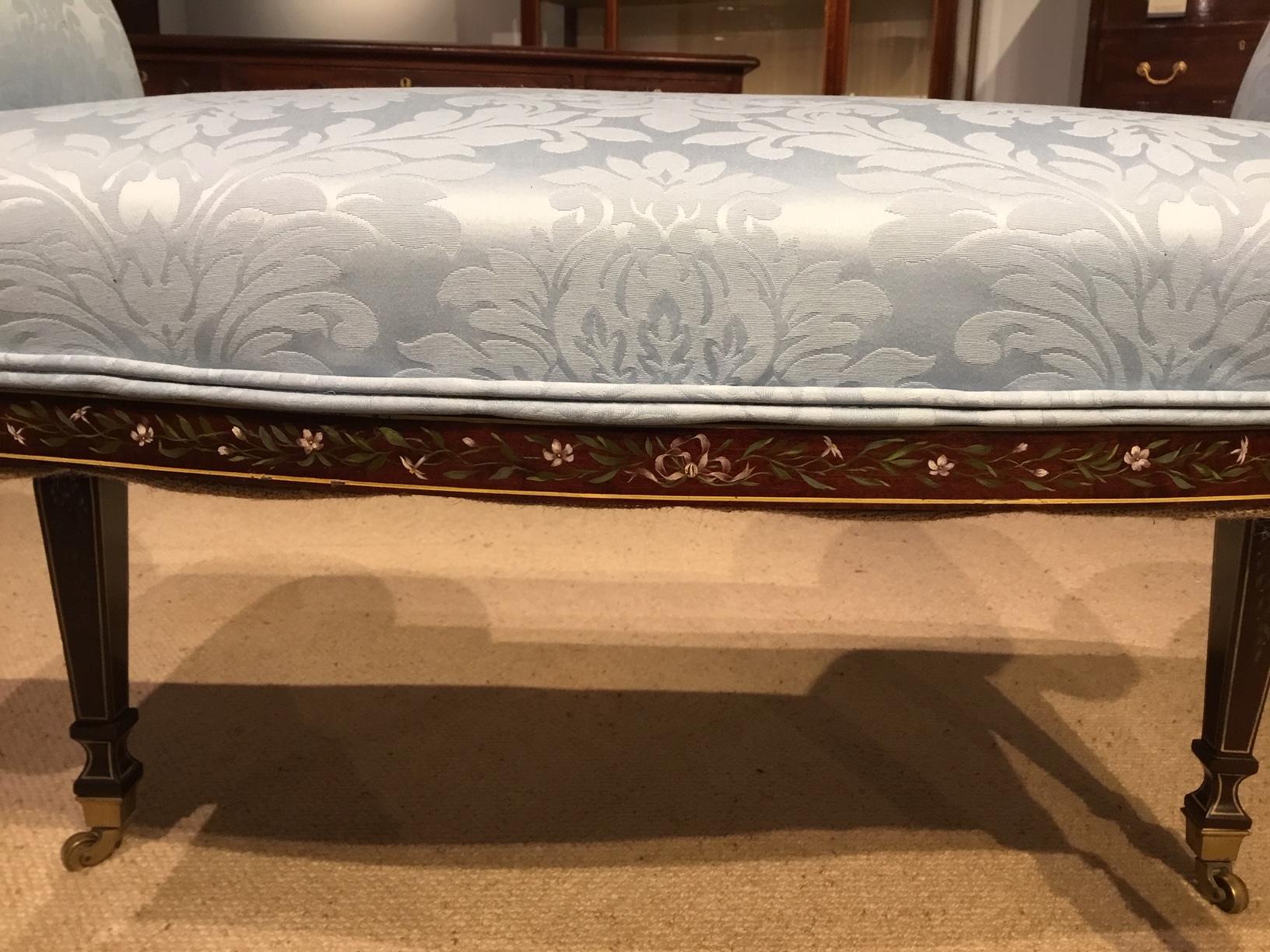 A mahogany polychrome Sheraton Revival window seat/stool. Having rolled padded ends, a sprung seat and Fine quality mahogany show frame with delicate hand painted floral detail with brass socket castors. Newly re-upholstered in a Sanderson's pale