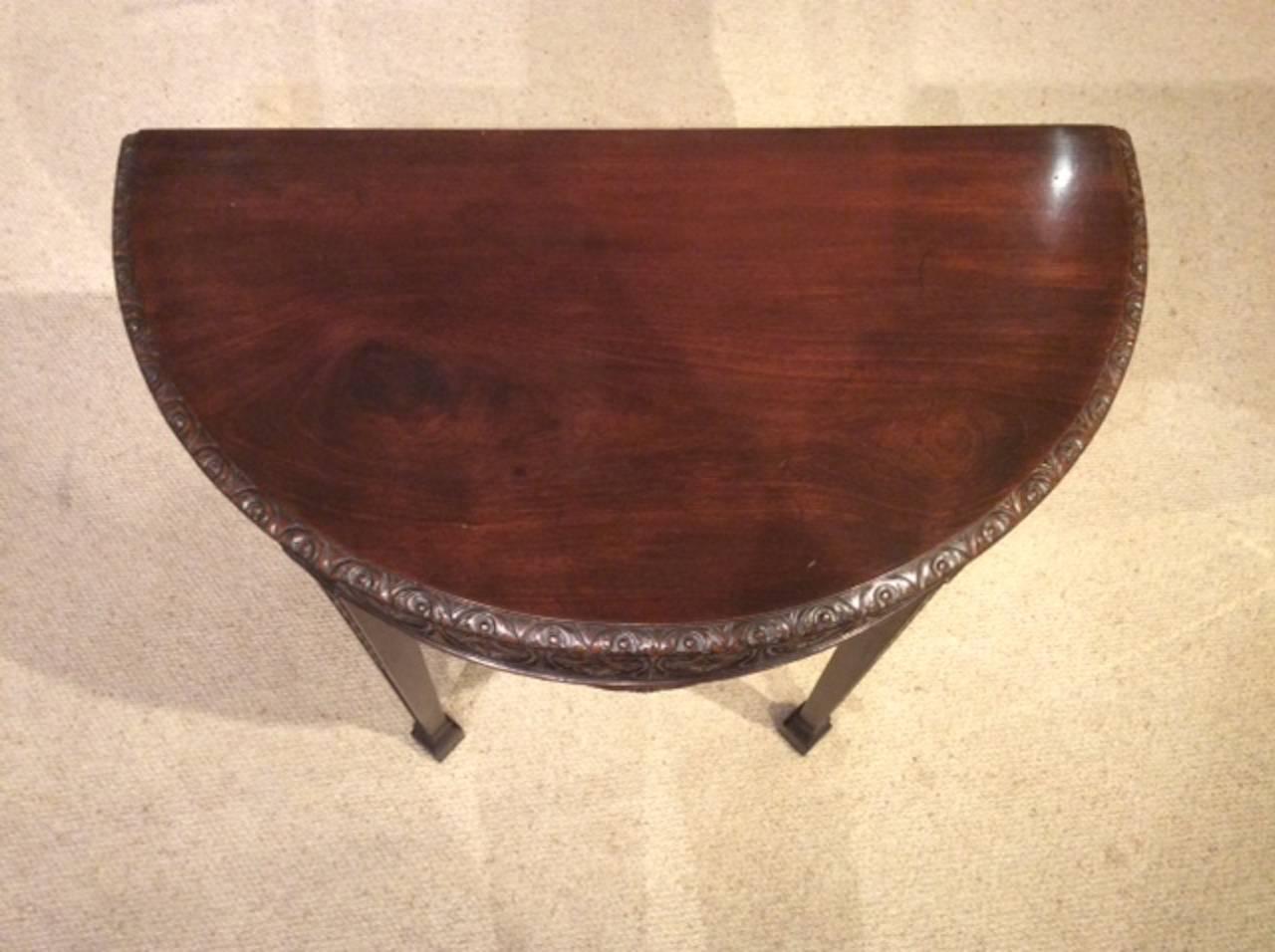 A mahogany Robert Adam design demilune side or console table. Having a solid mahogany top with a carved moulded edge, above a finely carved frieze with oval carved paterae. Supported on elegant square tapering supports with carved trailing harebells